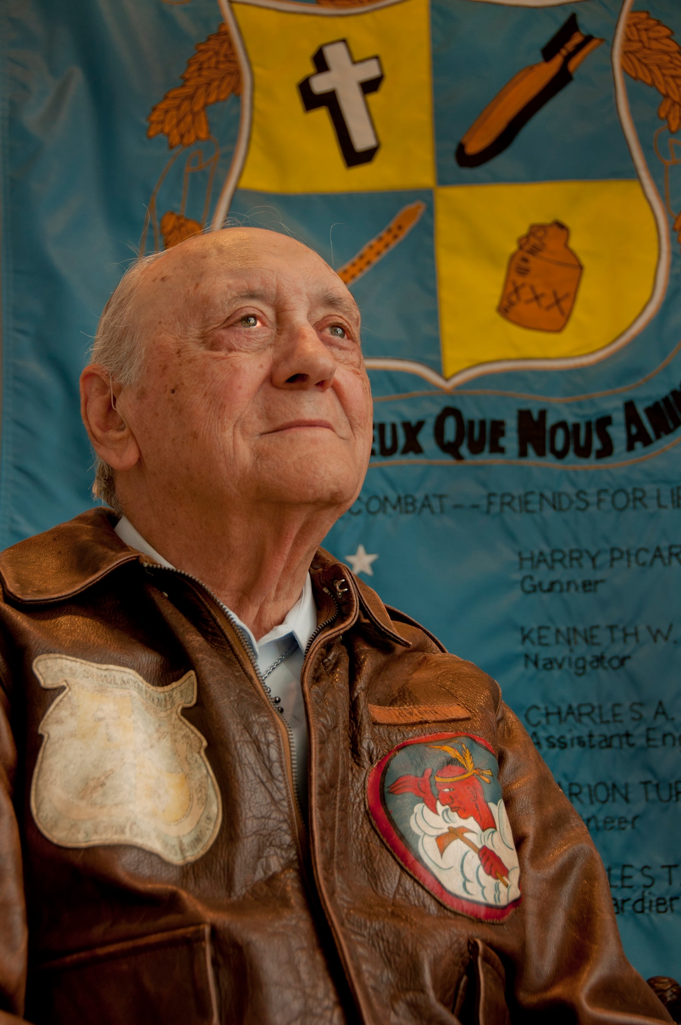 Lt. Col. (Ret.) Bill Getz sits in front of a rendition of the crew-designed crest that graced the B-24 Liberator he piloted during his D-Day missions. The aircraft was named The Phantom Renegade and the French motto roughly translates to "The Spirit of Those We Love." (U.S. Air Force photo/Senior Airman Madelyn Brown)
