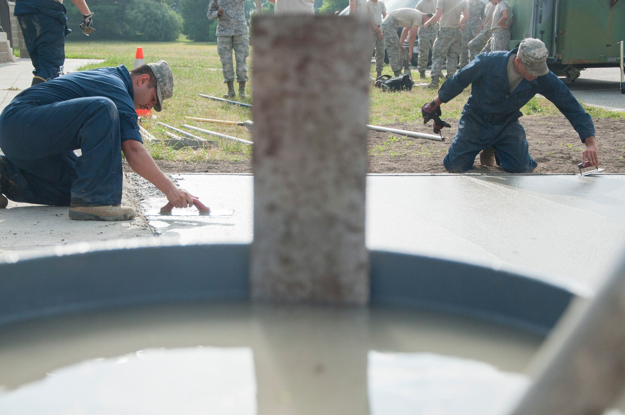 Two payment and equipment operators with the 436th Civil Engineer Squadron flatten fresh concrete June 25, 2014, on Dover Air Force Base, Del. Before the concrete was laid, combat arms instructors used a gravel driveway, which caused issues when loading and unloading ammunition. (U.S. Air Force photo/Senior Airman Jared Duhon)