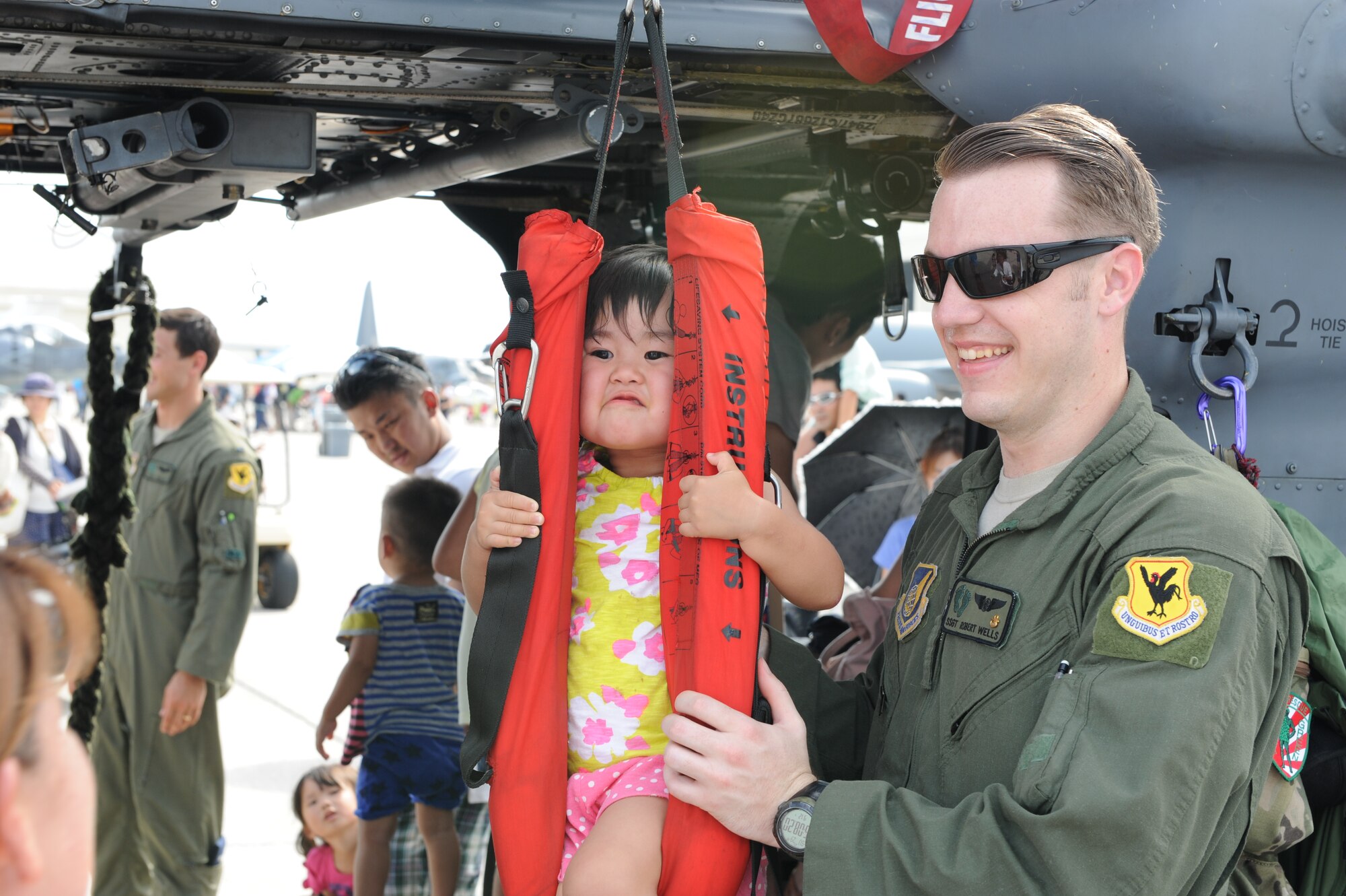 U.S. Air Force Staff Sgt. Robert Wells, assigned to the 33rd Rescue Squadron, shows a festivalgoer how to use a rescue sling on an HH-60 Pave Hawk helicopter on Kadena Air Base, Japan, June 29, 2014. The open house included musical guests, food and game booths and a wide variety of aircraft from the Air Force, Navy, Army, Marine Corps and Japan Air Self Defense Force. (U.S. Air Force photo by Airman 1st Class Stephen G. Eigel)