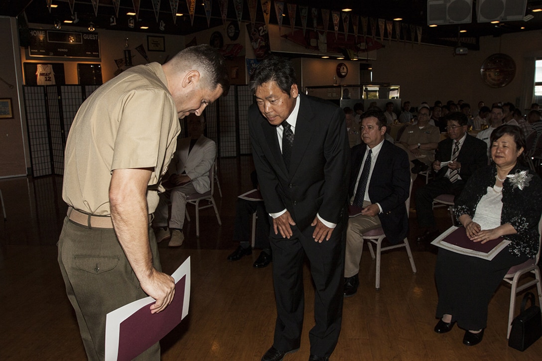 Col. Robert Boucher, Marine Corps Air Station Iwakuni, Japan, commanding officer, bows to a retiring Japanese employee during a retirement ceremony for Master Labor Contract and Independent Hire Agreement employees that took place in the Landing Zone inside Club Iwakuni Aboard Marine Corps Air Station Iwakuni, Japan, June 25, 2014.