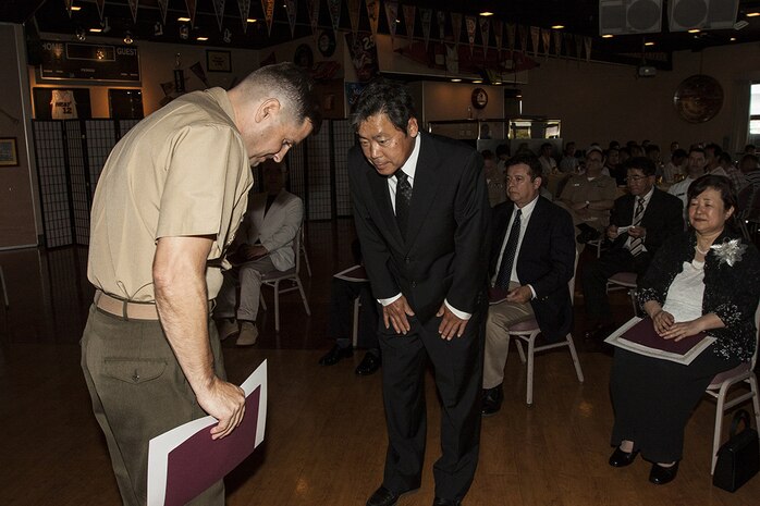 Col. Robert Boucher, Marine Corps Air Station Iwakuni, Japan, commanding officer, bows to a retiring Japanese employee during a retirement ceremony for Master Labor Contract and Independent Hire Agreement employees that took place in the Landing Zone inside Club Iwakuni Aboard Marine Corps Air Station Iwakuni, Japan, June 25, 2014.