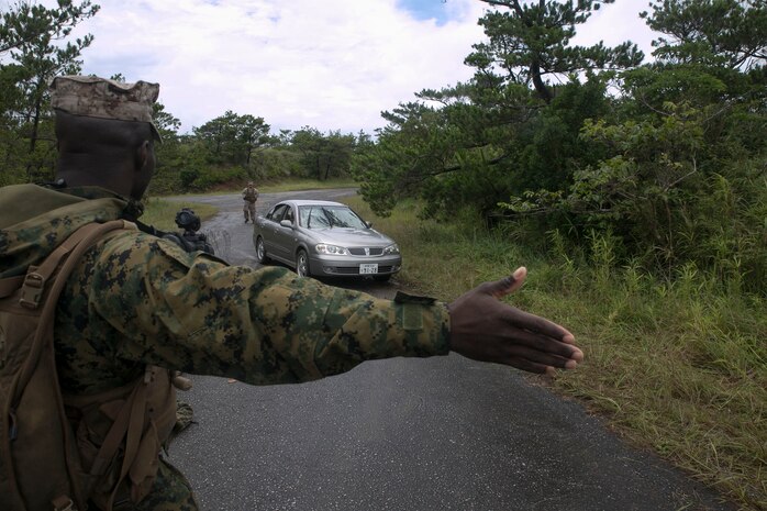 Cpl. Damion M. Gaskin directs a vehicle through a simulated checkpoint June 24 during Exercise Coral Thunder at Kadena Air Base. The vehicle checkpoint provided Marines an opportunity to train for different scenarios they may encounter during a deployment. Gaskin is a Bradenton, Florida, native and ground radio repairer with Marine Air Support Squadron 2, Marine Air Control Group 18, 1st Marine Aircraft Wing, III Marine Expeditionary Force.