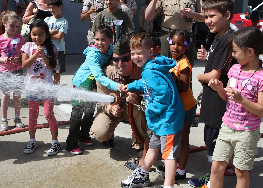 Cpl. Andrew Martinez, a crew chief with Aircraft Rescue and Firefighting, helps children operate a fire hose during a Lil’ Leatherneck day aboard Marine Corps Air Station Miramar, Calif., June 27. The Headquarters and Headquarters Squadron event served as an interactive tool for children to gain understanding about their parents’ military life.