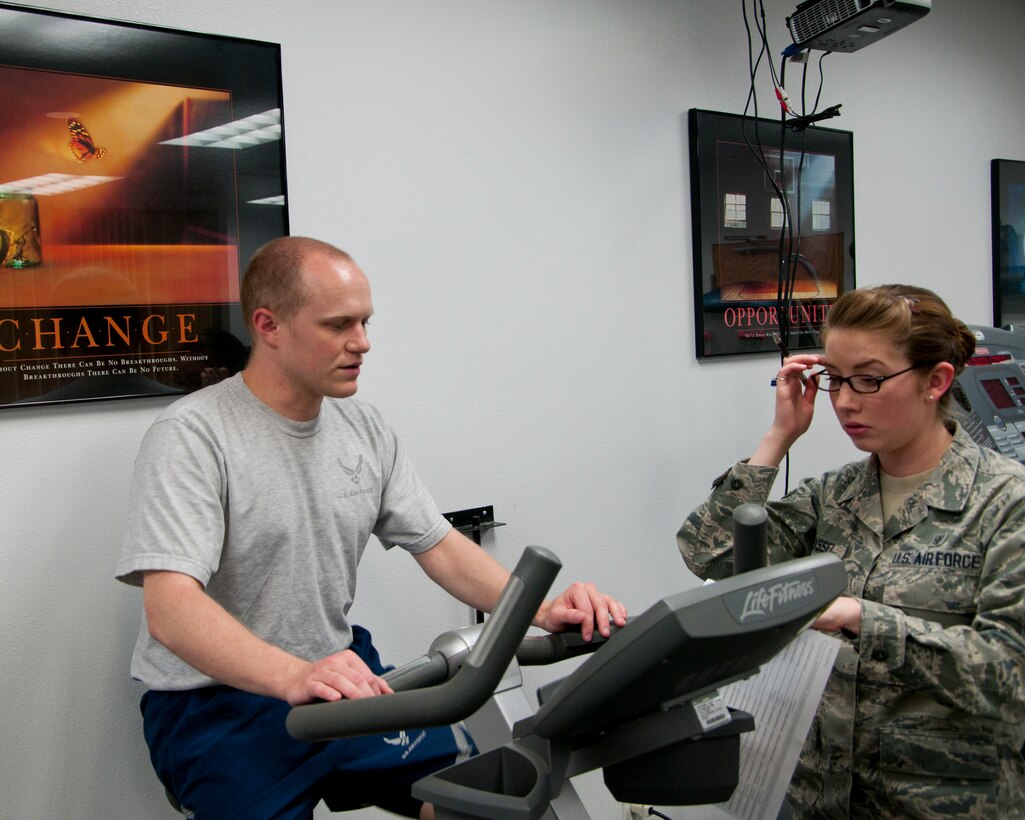 Staff Sgt. Eric Siebert, 90th Maintenance Operations Squadron data analyst, rides an exercise bike as part of his physical therapy while answering related questions from Airman 1st Class Felicia Grassel, 90th Medical Operations Squadron physical therapy technician, in the Freedom Hall Fitness Center June 25, 2014. Siebert is recovering from knee surgery. (U.S. Air Force photo by Airman 1st Class Jason Wiese)
