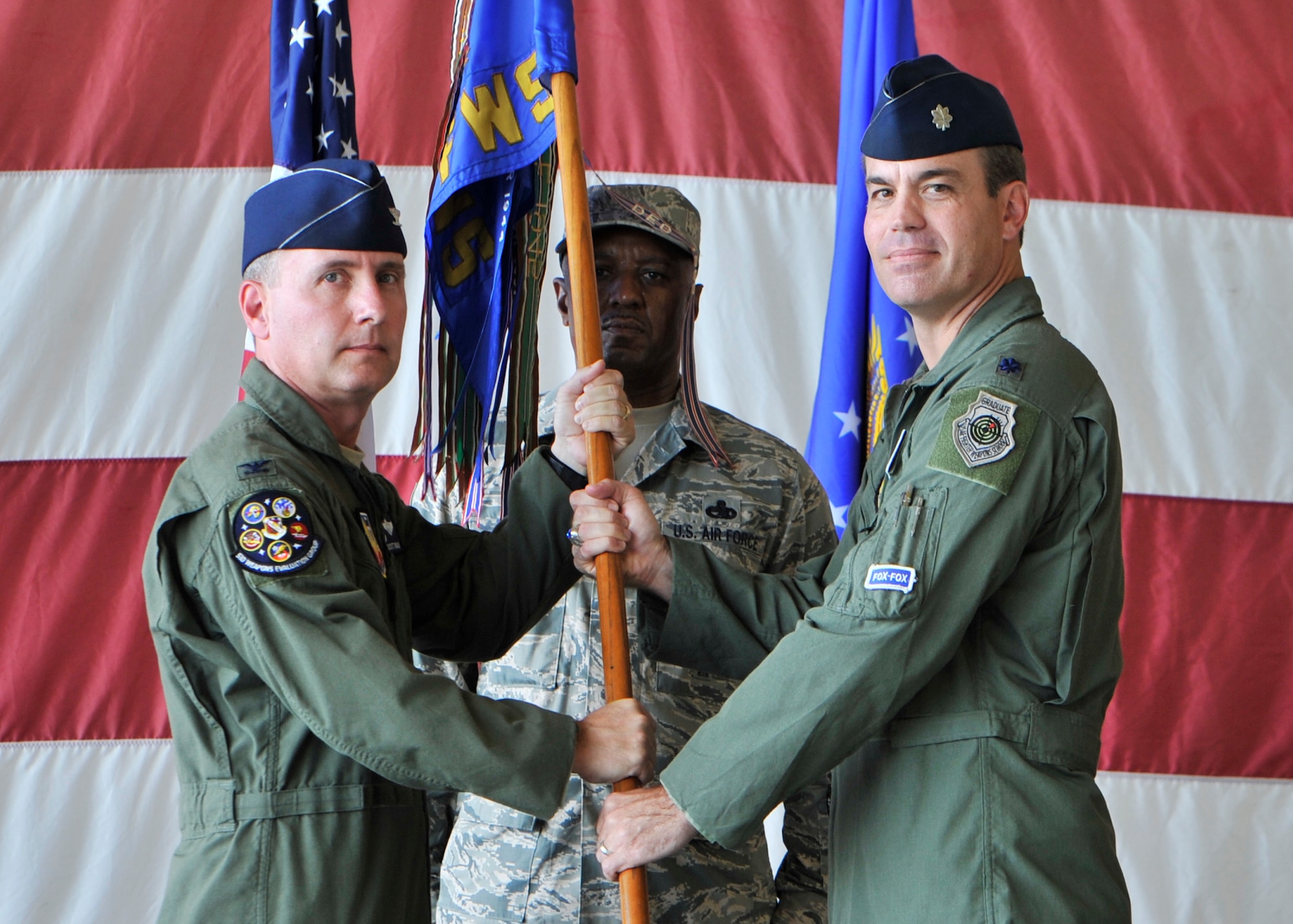 Colonel Scott Ward, 53rd Weapons Evaluation Group commander, passes the 83rd Fighter Weapons Squadron guidon to Lt. Col. Matthew Bradley who assumed command of the 83rd FWS in a change of command ceremony June 30, as Chief Master Sgt. John Thomas, 83rd FWS superintendent looks on. (U.S. Air Force photo by Airman 1st Class Sergio Gamboa)