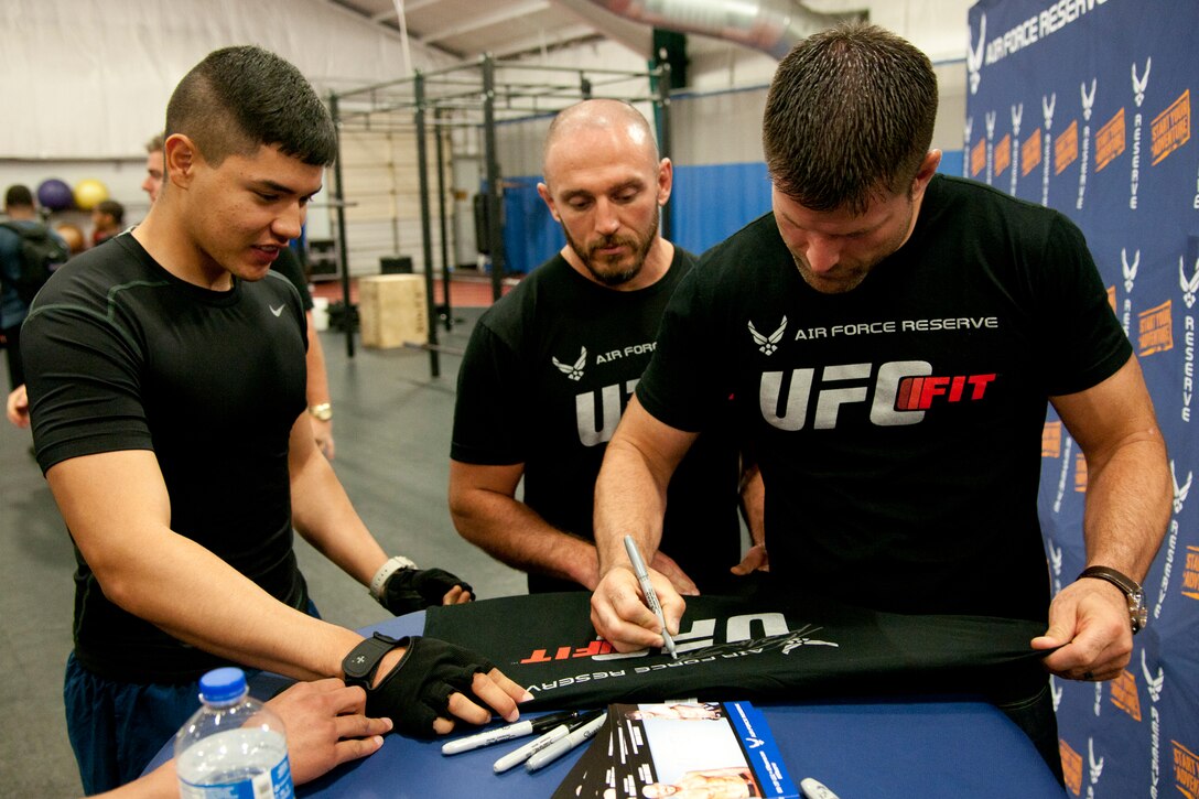 Mike Dolce, an Ultimate Fighting Championship FIT coach, and Brian Stann, a UFC fighter, veteran, and Silver Star recipient, sign autographs for a fan at the Tactical Fitness Center on Joint Base Andrews, Md., June 24, 2014. The UFC FIT program taught attendees about achieving maximum physical fitness through living a healthy lifestyle, and was sponsored by the Air Force Reserve. (U.S. Air Force photo/Airman 1st Class J.D. Maidens)