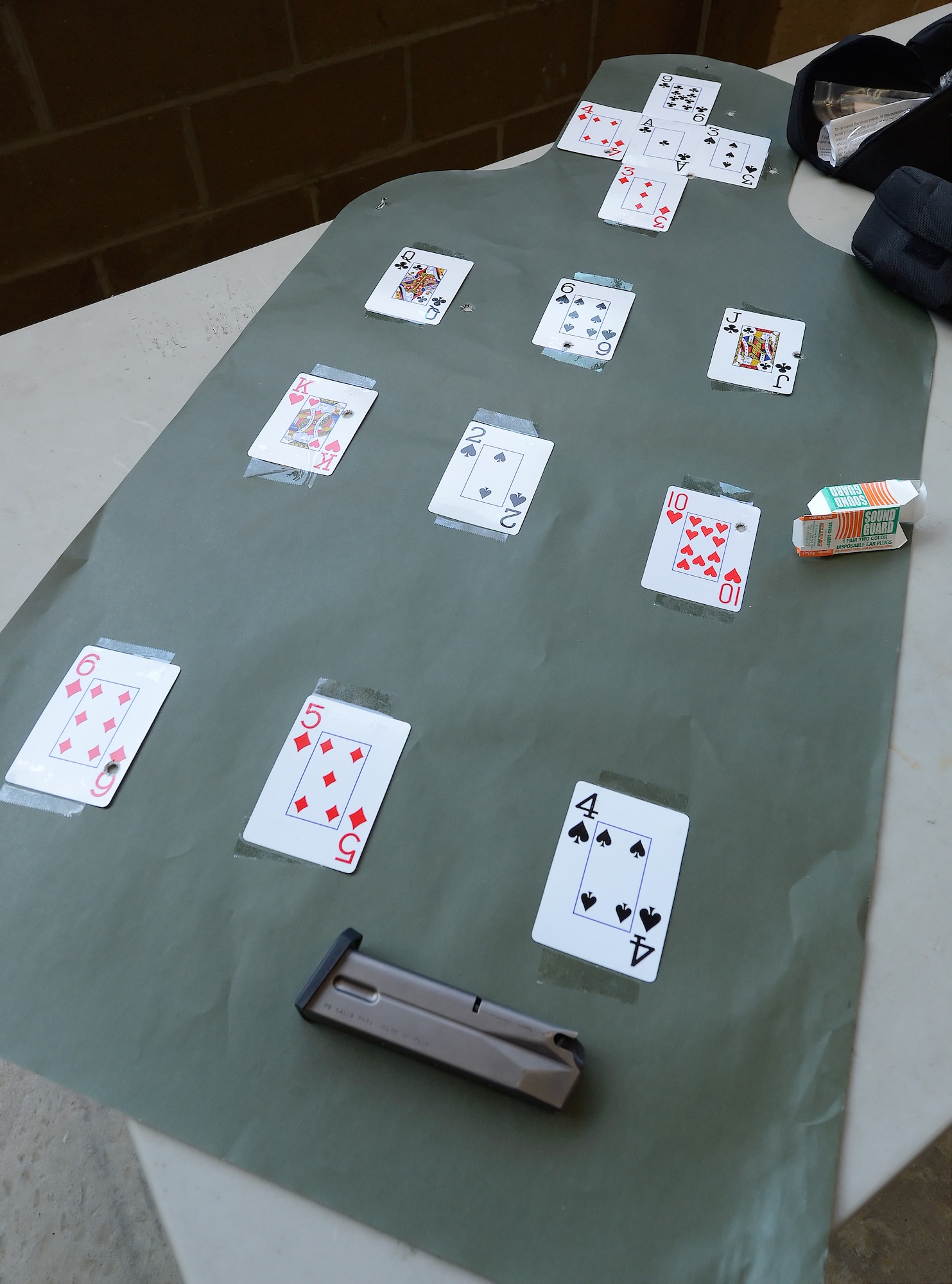 Elements from a shooting competition between senior leadership of the 436th Airlift Wing sit on a table after the competition ended June 20, 2014, at Dover Air Force Base, Del. Shown on the table is a paper target with playing cards, an empty magazine for a 9 mm Beretta pistol, a box for earplugs, and cases for protective eyewear. (U.S. Air Force photo/Greg L. Davis)