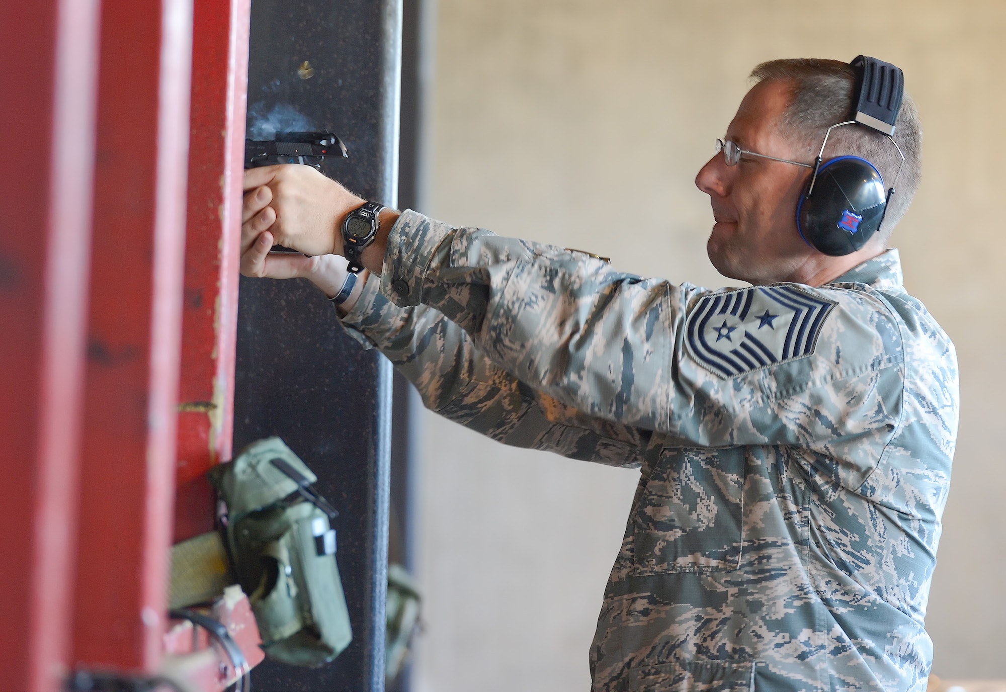 Hot-gasses and a brass shell exit a 9 mm pistol after being fired by Chief Master Sgt. Stanley C. Cadell, 436th Airlift Wing command chief, during a senior leaders??? shooting competition June 20, 2014, at Dover Air Force Base, Del. Cadell wears hard-shell hearing protection. The competition was held at the Dover AFB Combat Arms and Maintenance Training range. (U.S. Air Force photo/Greg L. Davis)