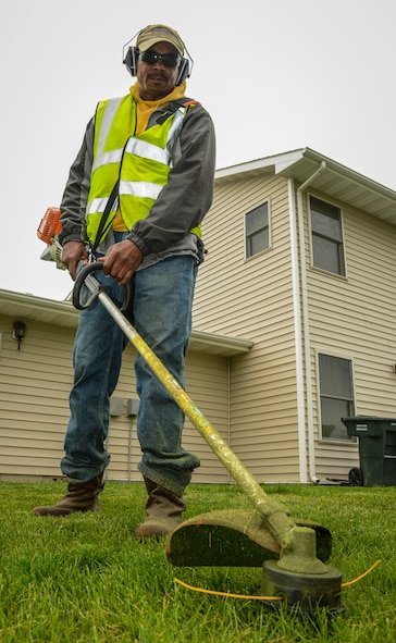 Johnathan Jackson, a contractor working for Balfour Beatty Communities, uses a weed-whacker to trim grass near a residence in housing on Minot Air Force Base, N.D., June 13, 2014. According to the BBC residents guide, residents in housing are responsible for watering the lawn trees and shrubs that surround their home as well as mowing their back yard, if they have a fence, and trimming their fence lines. (U.S. Air force photo/Senior Airman Stephanie Morris)