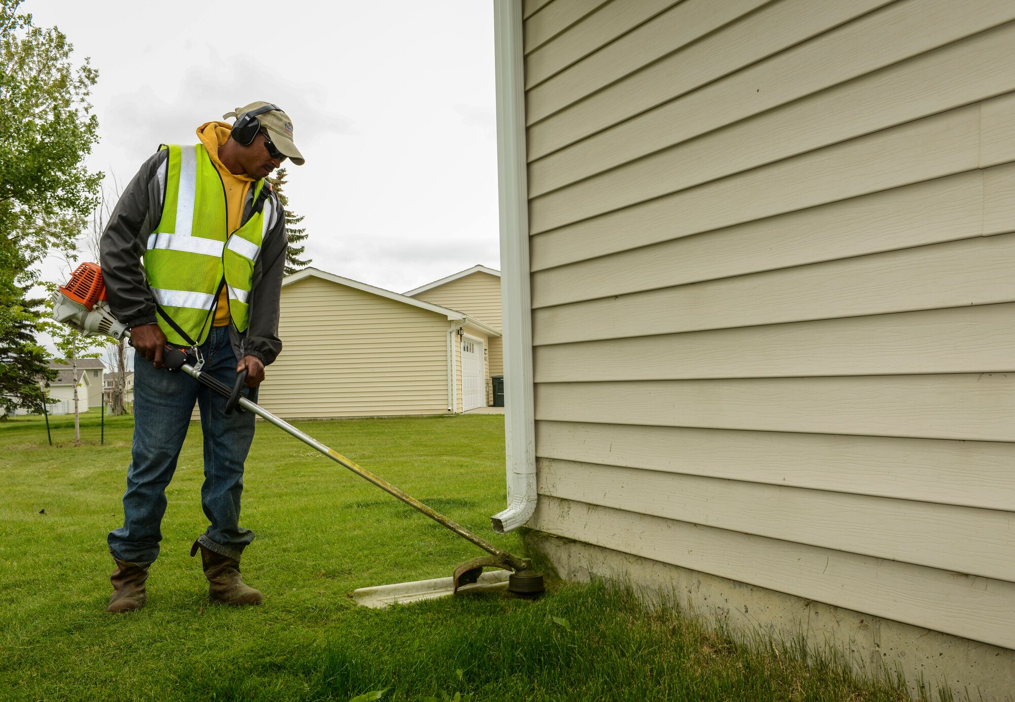 Johnathan Jackson, a contractor working for Balfour Beatty Communities, uses a weed-whacker to trim grass near a residence in housing on Minot Air Force Base, N.D., June 13, 2014. During the summer months, on base, seasonal rules regarding lawn care, recycling, curfews for minors, yard sales, parking and holidays go into effect in the BBC housing community. (U.S. Air force photo/Senior Airman Stephanie Morris)