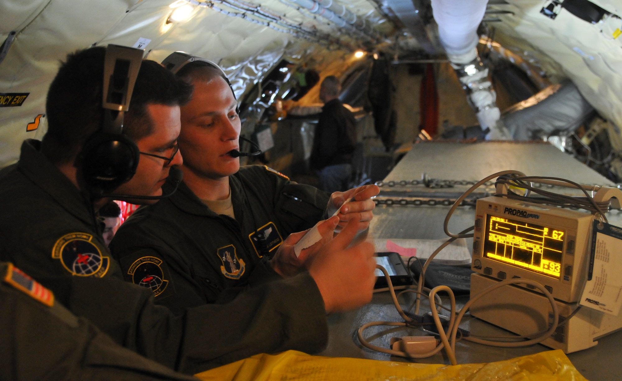 U.S. Air Force Tech. Sgt. Daniel Nelson, left, and Senior Airman John Leithead, right, both assigned to the 775th Expeditionary Aeromedical Evacuation Flight, Joint Base Andrews, Md., review a wounded service member’s vital signs while monitoring the patient’ s heart rate and oxygen levels during the aeromedical transport of patients from Joint Base Andrews to Marine Corps Air Station Miramar, San Diego, aboard a KC-135 Stratotanker assigned to the 128th Air Refueling Wing, Milwaukee, Jan. 13, 2014. The two Airmen are part of the five-person EAEF team aboard the KC-135 in support of a total force integration aeromedical evacuation mission. (U.S. Air National Guard photo by Staff Sgt. Jeremy Wilson/Released)