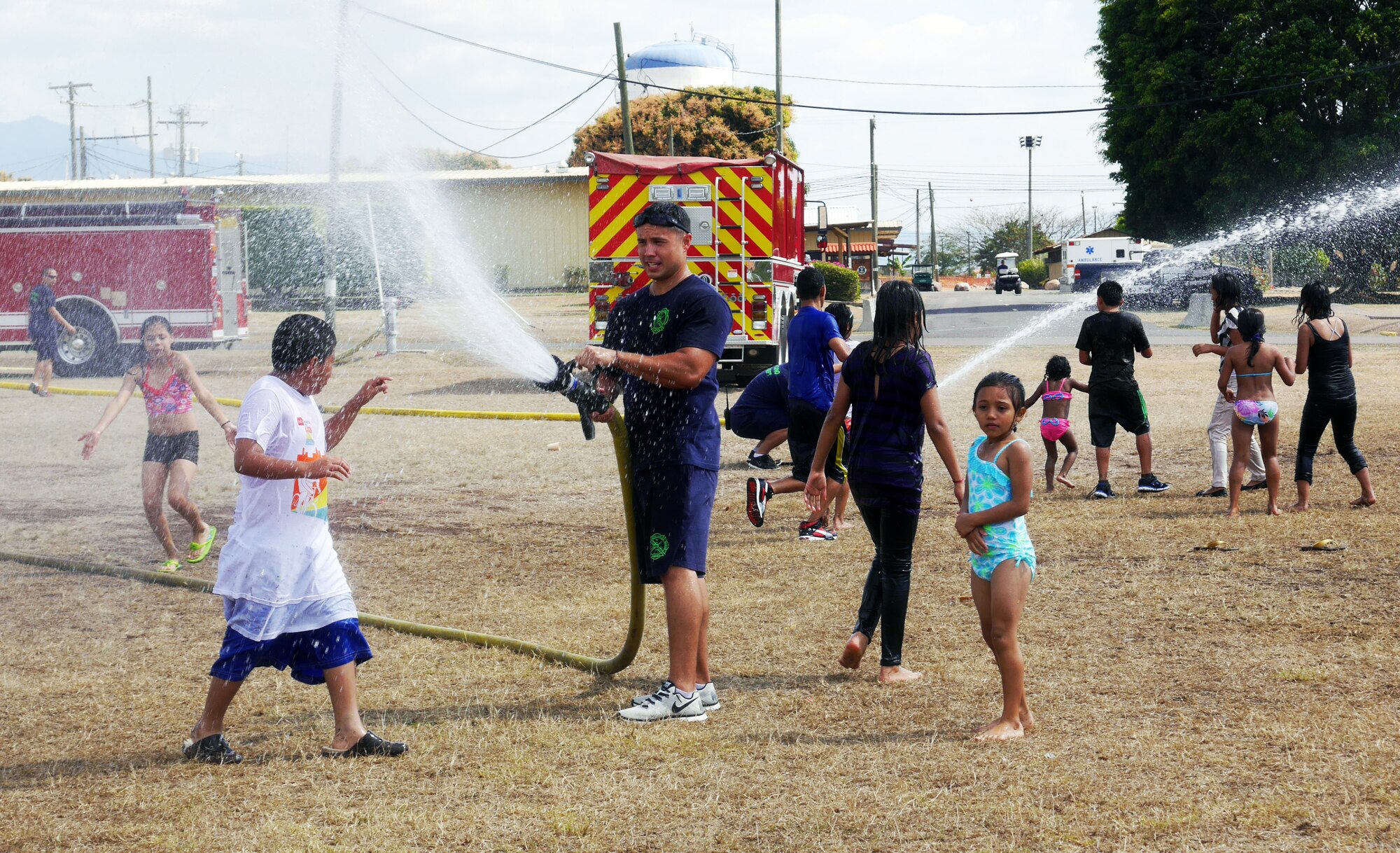 Firefighters from the 612th Air Base Squadron spray water for children to play in during a "Fiesta Day" at Soto Cano Air Base, Honduras, March 1, 2014.  Joint Task Force-Bravo's Medical Element (MEDEL) hosted a “Fiesta Day” for 40 boys, 72 girls, and 23 adult chaperones from the Hogar de Ninos and Ninas Nazareth orphanages.  The “Fiesta Day” was a way for the current MEDEL to say farewell to the children they have been supporting as their nine-month tour at Soto Cano draws to a close.  (Photo by U.S. Army Sgt. Courtney Kreft) 
