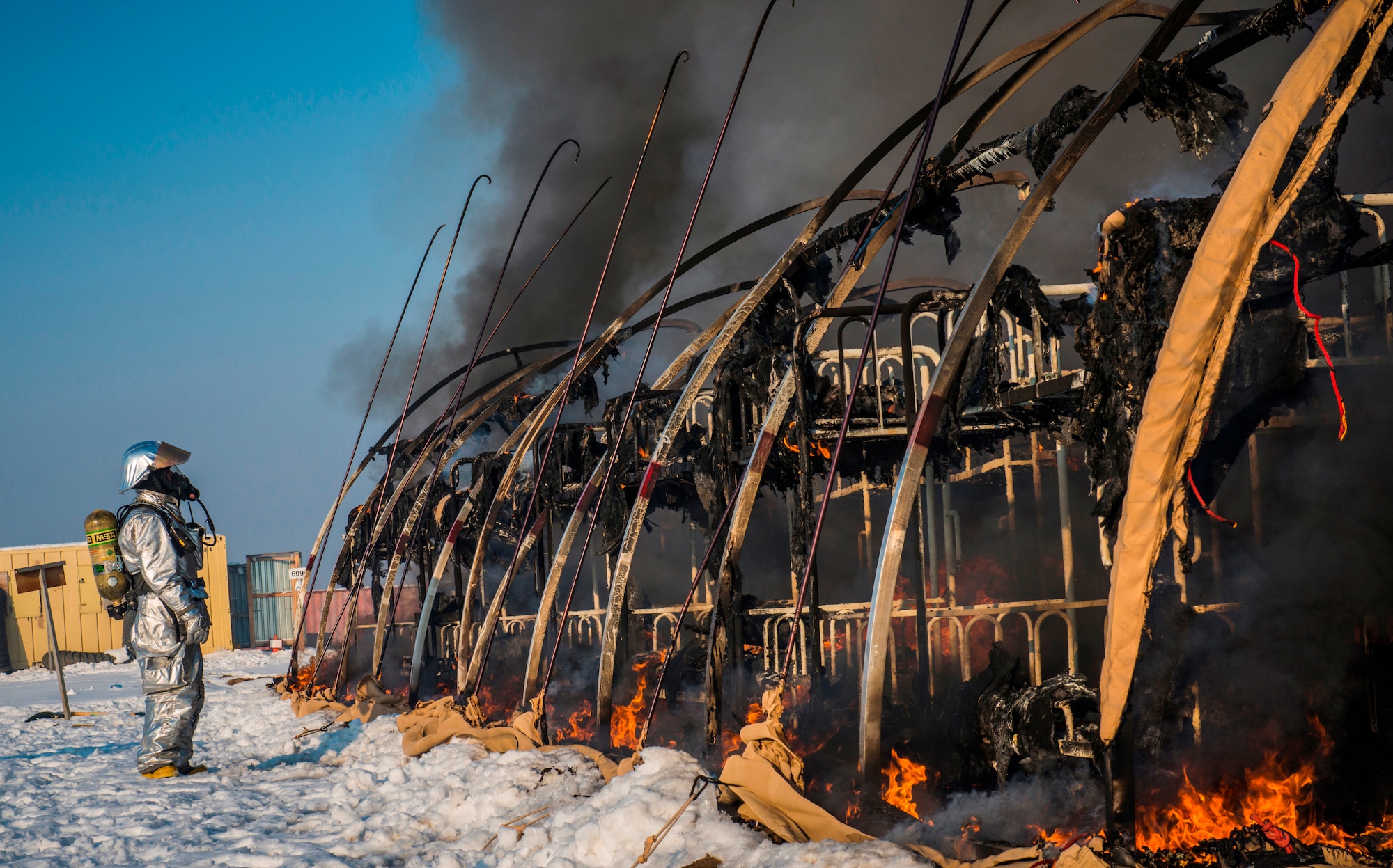 A firefighter with the 376th Expeditionary Civil Engineer Squadron asssesses thestatus of the remaining fire during a training event at Transit Center at Manas, Kyrgyzstan, March 1, 2014. The 376th ECES used the training to demonstrate how fast the tents burn: In this case, approximately two and a half minutes. The transient tent was the last in Hotel Alaska, marking another step in closing the facility and removing U.S. troops from the Transit Center by July 11, 2014. (U.S. Air Force photo/Staff Sgt. Travis Edwards) 