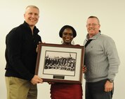 Col. Terri Bailey, 319th Medical Group commander (middle), presents a portrait of the Tuskegee Airmen to Col. Paul Bauman, 319th Air Base Wing commander (left), Chief Master Sgt. David Duncan, 319th Air Base Wing command chief (right) to be accepted on behalf of the 319th Air Base Wing as a whole, Feb. 28, 2014, at the Northern Lights Club ballroom on Grand Forks Air Force Base, N.D. Bailey wanted the gift to display how the Air Force is progressing and engraved on it is, “Move forward but never forget.” (U.S. Air Force photo/Airman 1st Class Zachiah Roberson