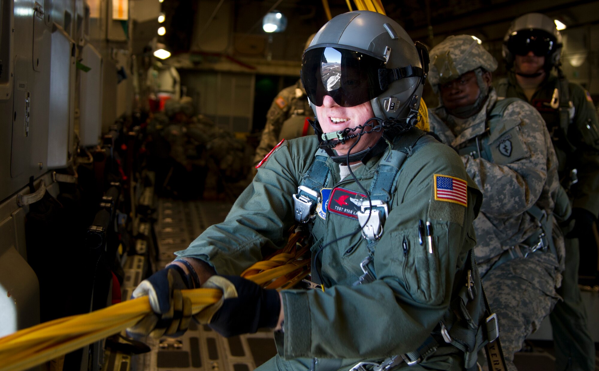 Tech. Sgt. Ryan Eads and Army Maj. Jeffrey Munn pull static lines back into the aircraft while Senior Airman Kelly Bollinger prepares to assist Eads and Munn, Feb. 27, 2014, over Malemute Drop Zone at Joint Base Elmendorf-Richardson, Alaska. The static line is a cord attached at one end to the aircraft and at the other to the Soldier’s parachute container, and that extracts the T-11 parachute. (U.S. Air Force photo/Staff Sgt. Sheila deVera)