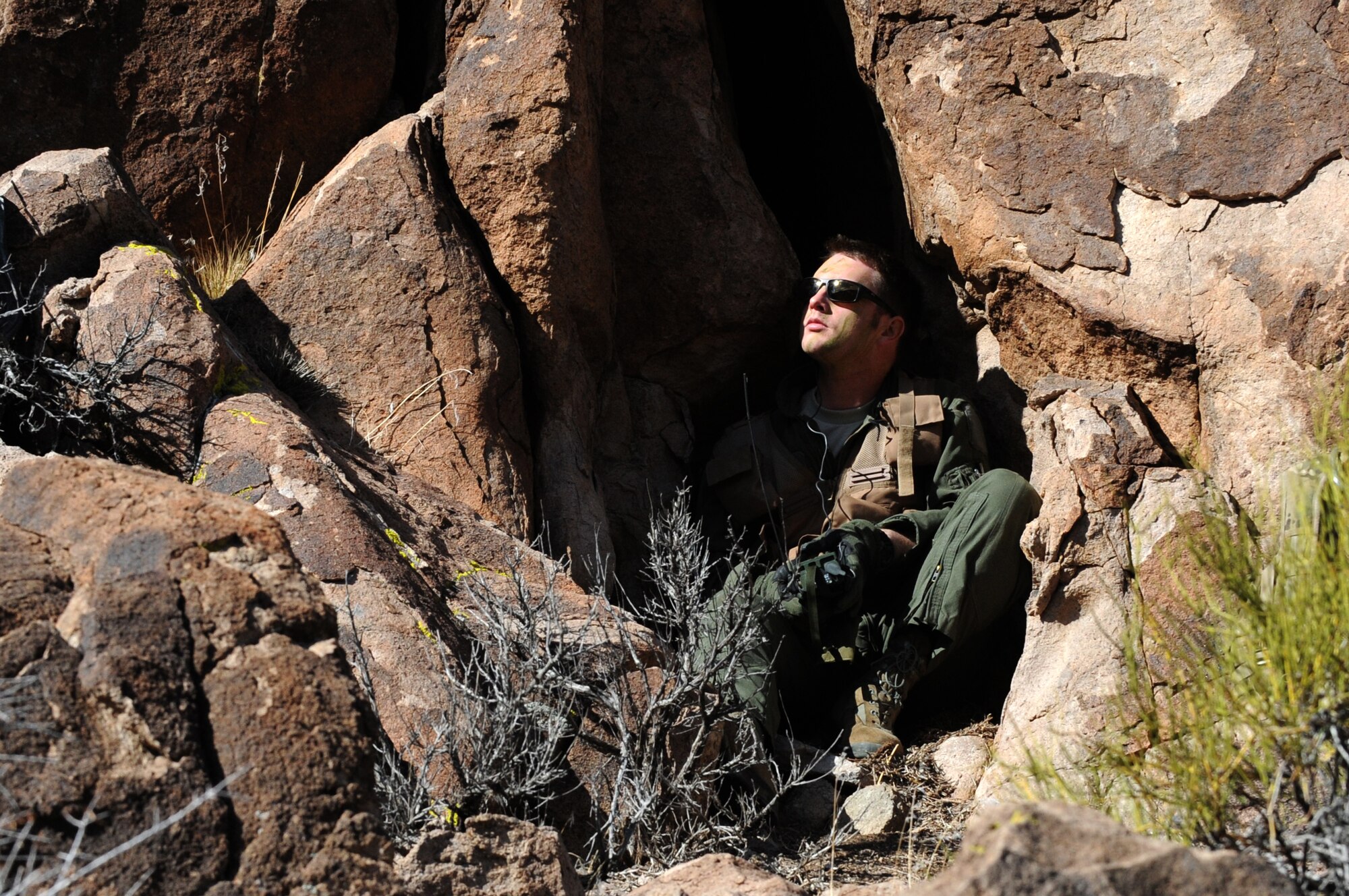Holed up in a mountain rock formation, U.S. Air Force 1st Lt. Ryan Gipson, 336th Fighter Squadron F-15E Strike Eagle pilot, checks for “enemy forces” on a Southern Nevada range March 4, 2014, during Red Flag 14-2. Gipson scaled boulders, forged brush and battled the elements to elude capture while awaiting rescue. (Air Force photo/Staff Sgt. Chuck Broadway)