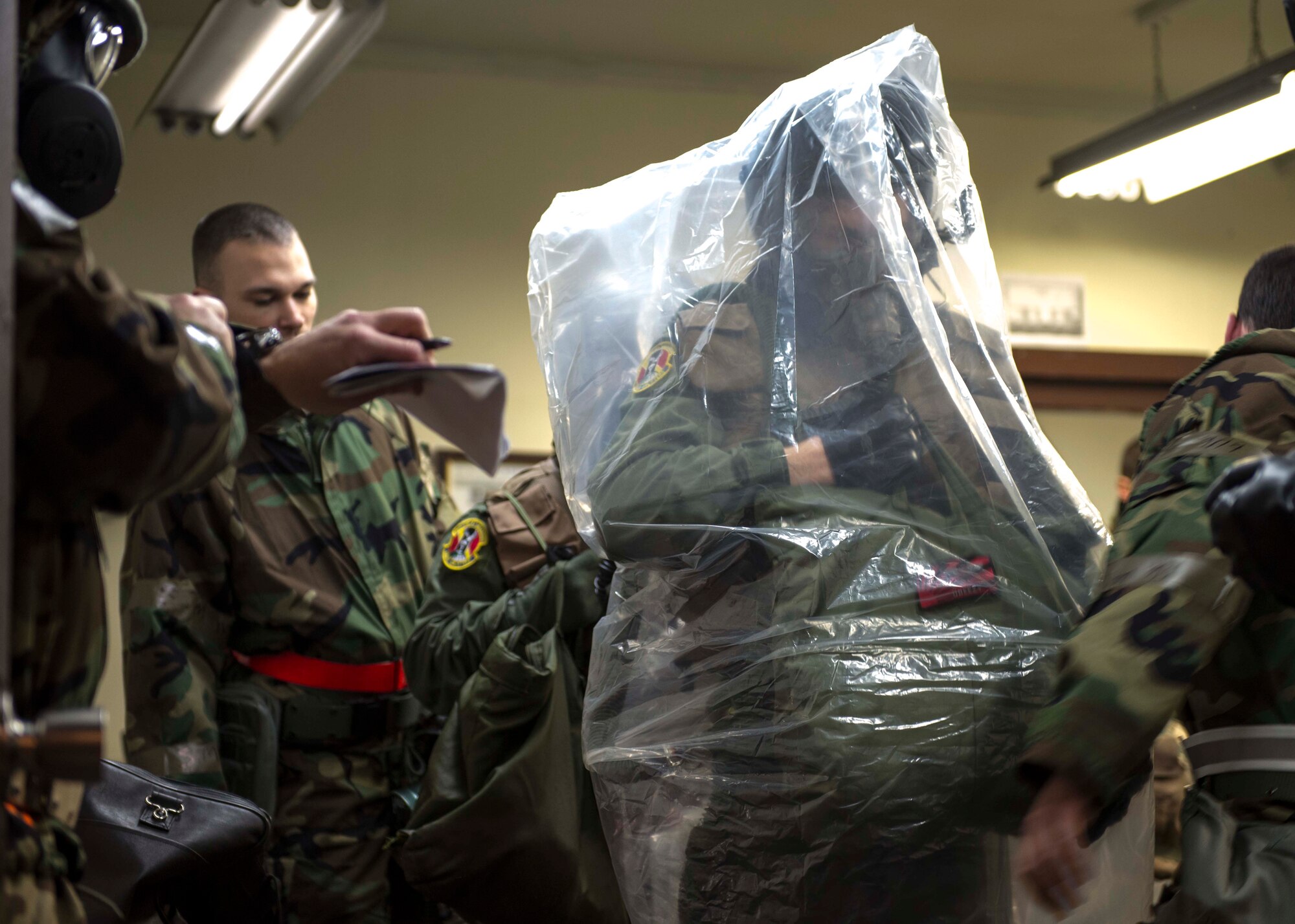 An Airman dons an over cape over his aircrew chemical defense ensemble during the Samurai Readiness Inspection at Yokota Air Base, Japan, March 5, 2014.  The over cape is worn during the hazard deposition phase of an attack.  (U.S. Air Force photo by Airman 1st Class David Danford / released)