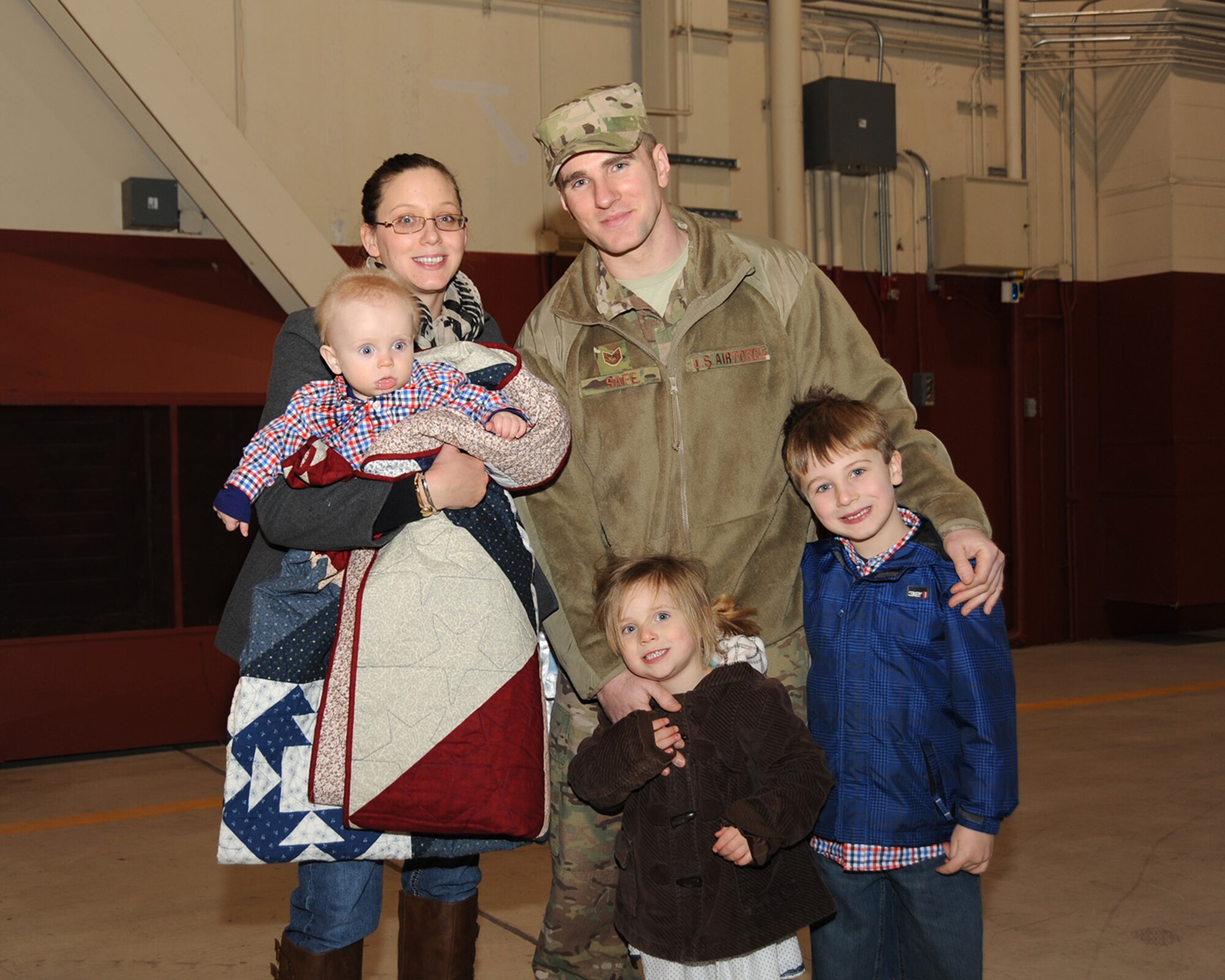 While bundled up with a quilt made by the Mid Valley Quilt Guild, Tech. Sgt. Ken Safe and his family pose for a photo following the mobilization ceremony held at the Portland Air National Guard Base, Ore., March 1. (Air National Guard photo by Master Sgt. Shelly Davison, 142nd Fighter Wing Public Affairs/Released) 