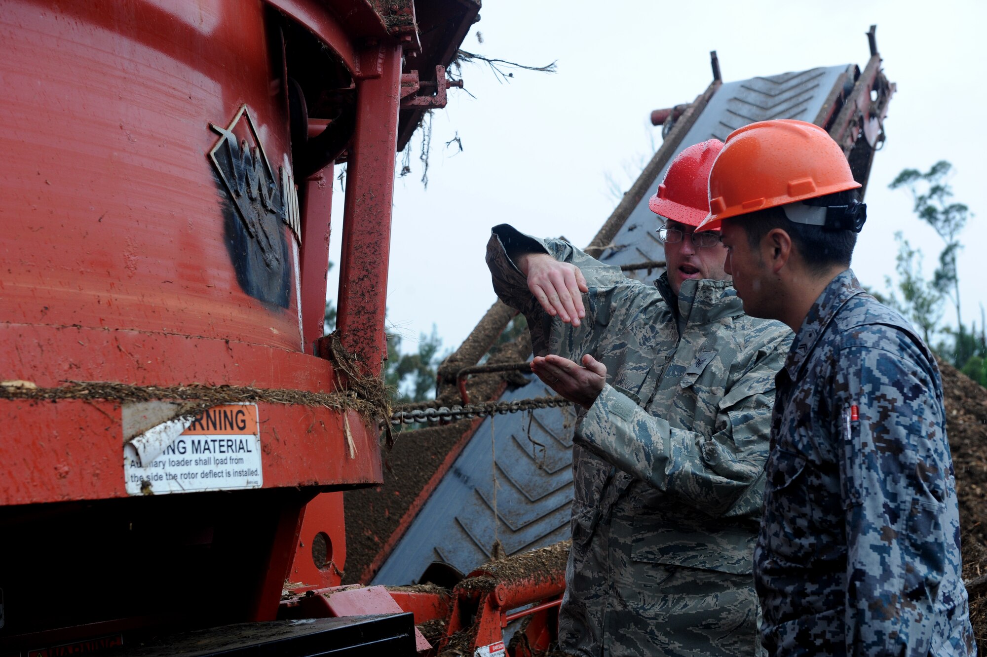 U.S. Air Force Staff Sgt. Paul Mitchell, 18th Civil Engineer Squadron pavements and equipment craftsmen, explains how to fold the conveyor belt of a Morbark Tub Grinder to Japan Air Self-Defense Force Tech. Sgt. Tatsuya Tsuruta, civil engineer construction worker, on Kadena Air Base, Japan, March 4, 2014. The conveyor belt shoots small pieces of wood into a pile after it has been ground by the machine, creating mulch. (U.S. Air Force photo by Airman 1st Class Hailey R. Staker)