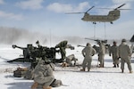 A CH-47 Chinook with a slingloaded M-777 155mm howitzer flies overhead as Soldiers with the Michigan Army National Guard’s 1st Battalion, 119th Field Artillery Regiment, use picks to remove inches of ice in order to set up their howitzers during a live fire exercise at Camp Grayling Joint Maneuver Training Center, Mich. Soldiers from the battalion conducted training on cold weather and slingload operations, transporting, setting up and firing their howitzers in temperatures that got down to -30 degrees