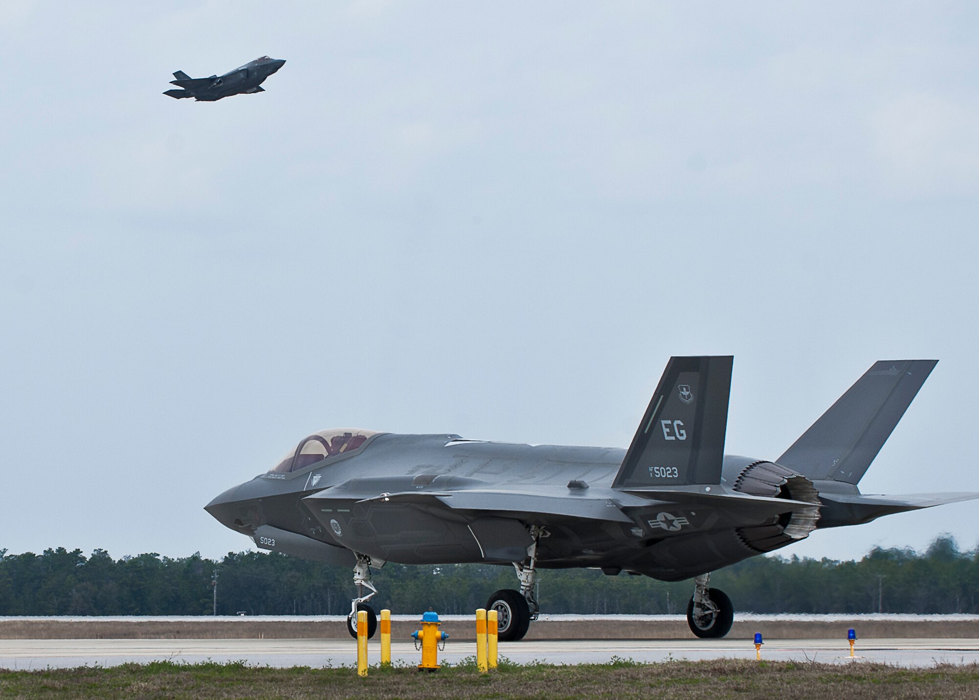 A 33rd Fighter Wing F-35A Lightning II taxis back after a sortie as another F-35 lifts off from Eglin Air Force Base, Fla.  (U.S. Air Force photo/Samuel King Jr.)