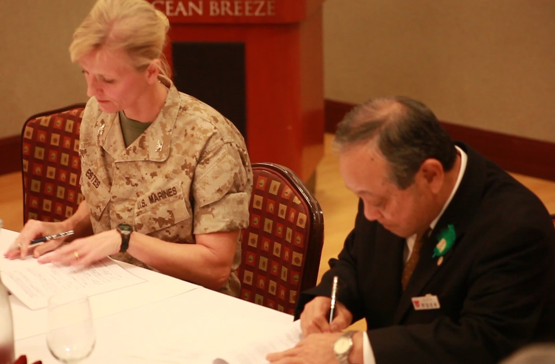 Mayor Masaharu Noguni, right, and Col. Katherine J. Estes sign an agreement at the Ocean Breeze here March 11 detailing the standard operating procedures for the Local Implementing Agreement. The LIA allows Camp Foster to open its gates to provide evacuees immediate and direct passage to higher ground or shelter immediately before, during or after a natural disaster. All in attendance observed a moment of silence to remember the victims and reflect upon the impact of the Great East Japan Earthquake and subsequent tsunami, which struck Japan on this date in 2011. The earthquake and tsunami are among the most destructive natural disasters in Japan’s history. The signing is a critical step to help safeguard the citizens of local communities and reaffirms the commitment of the U.S. to help its neighbors. Noguni is the mayor of Chatan, and Estes is the commanding officer of Headquarters and Service Battalion, Marine Corps Base Camp Smedley D. Butler, and Camp Foster. 