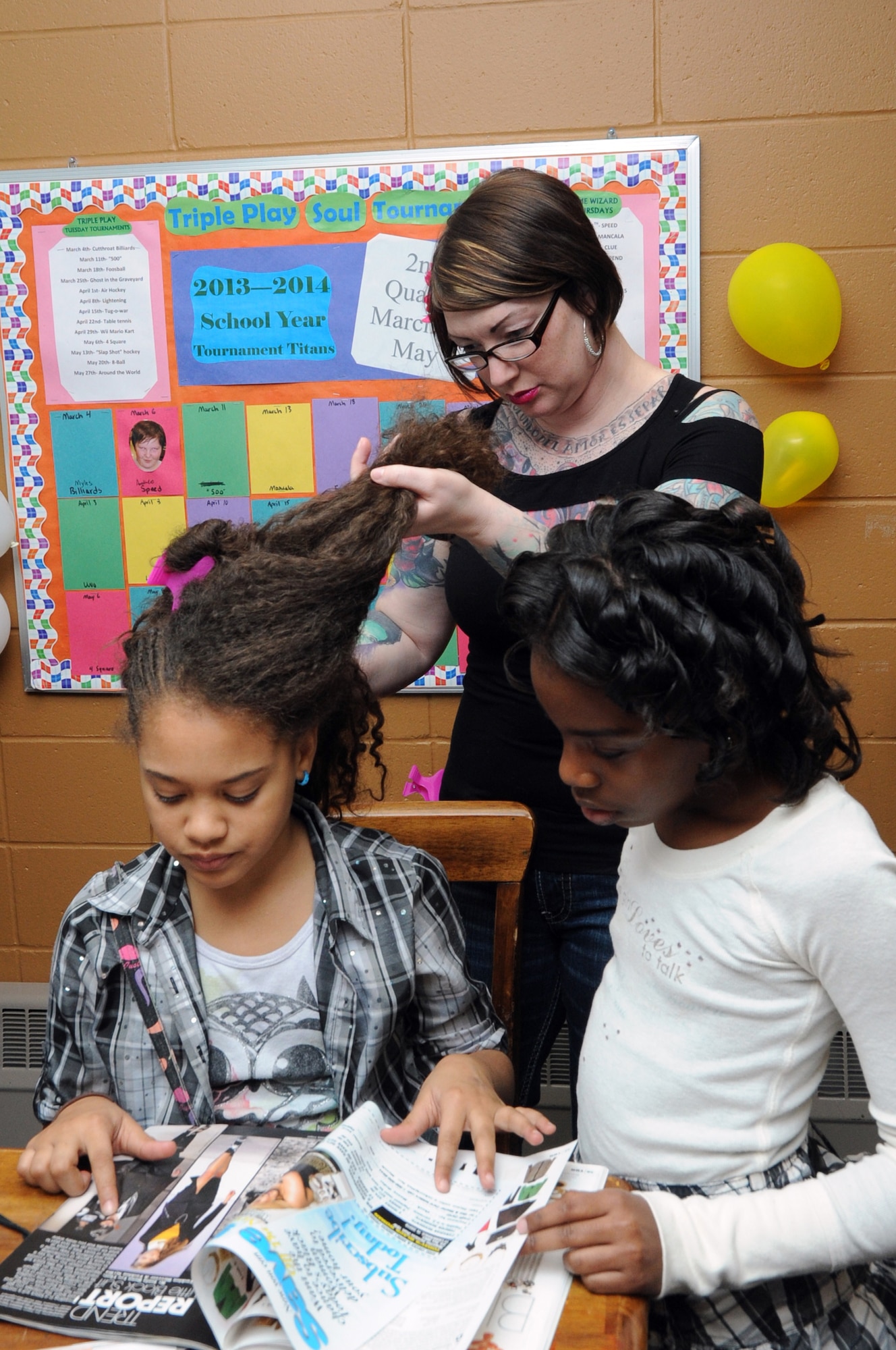 Staff Sgt. Melissa Booker, 319th Contracting Flight contract specialist, styles Camille Pettigrew's hair while she and her friend Emelia Hay browse a fashion magazine at the 319th Force Support Squadron Prom Prep Academy event at the Youth Center on Grand Forks Air Force Base, N.D., March 8, 2014. While high school-age girls tried on donated prom dresses, younger girls learned about makeup and hairstyles from volunteers. (U.S. Air Force photo/Staff Sgt. David Dobrydney)