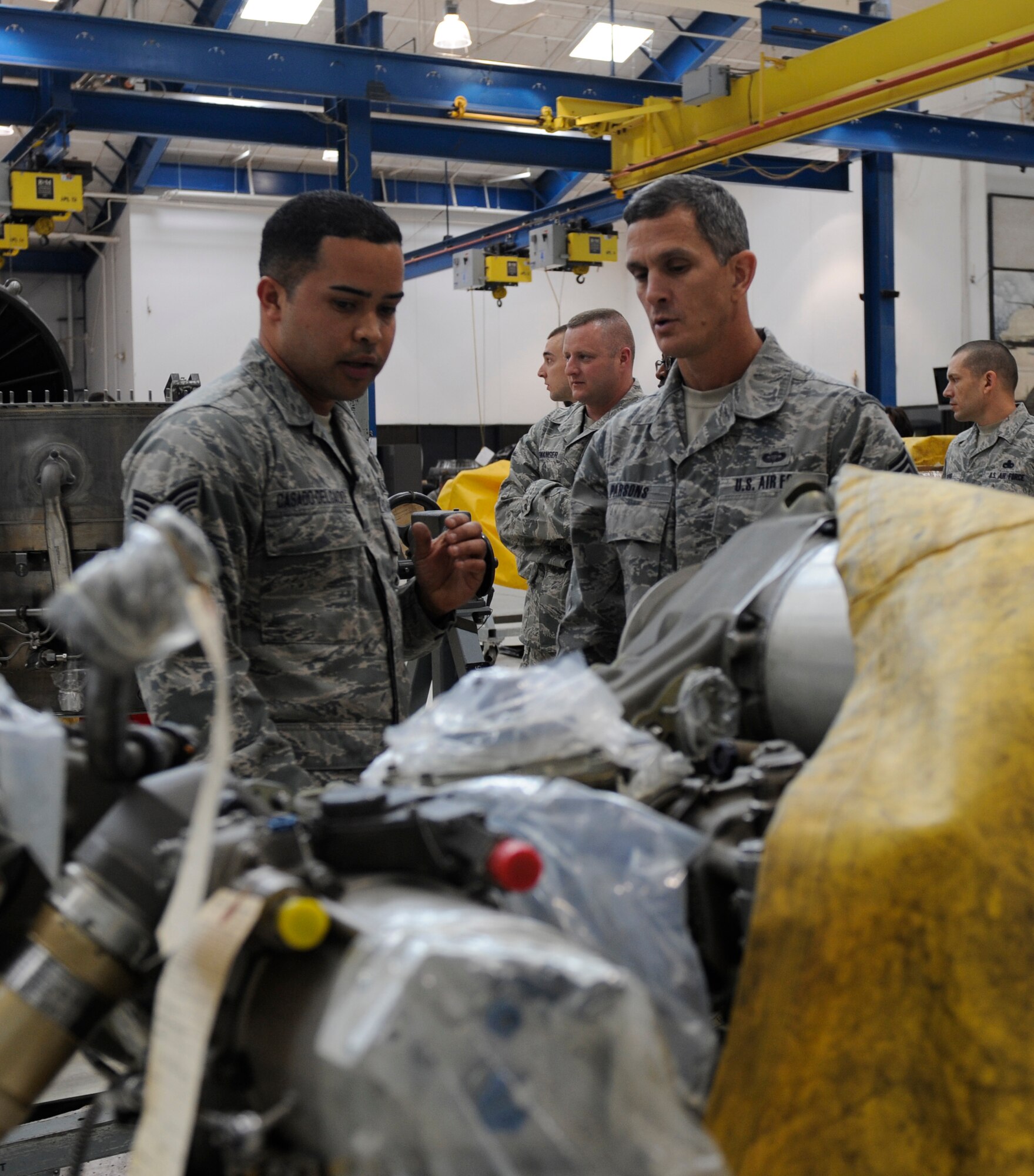 U.S. Air Force Senior Airman Hector Casado-Delgado, left, 7th Maintenance Group propulsion technician, explains to Chief Master Sgt. Richard Parsons, Air Combat Command command chief, how a fuel component  on a B-1B Lancer engine operates March 5, 2014, at Dyess Air Force Base, Texas. Casado-Delgado explained the inner workings of the engine shop to Parsons as he led him and his party on a tour of his workcenter. (U.S. Air Force photo by Airman 1st Class Alexander Guerrero/Released)