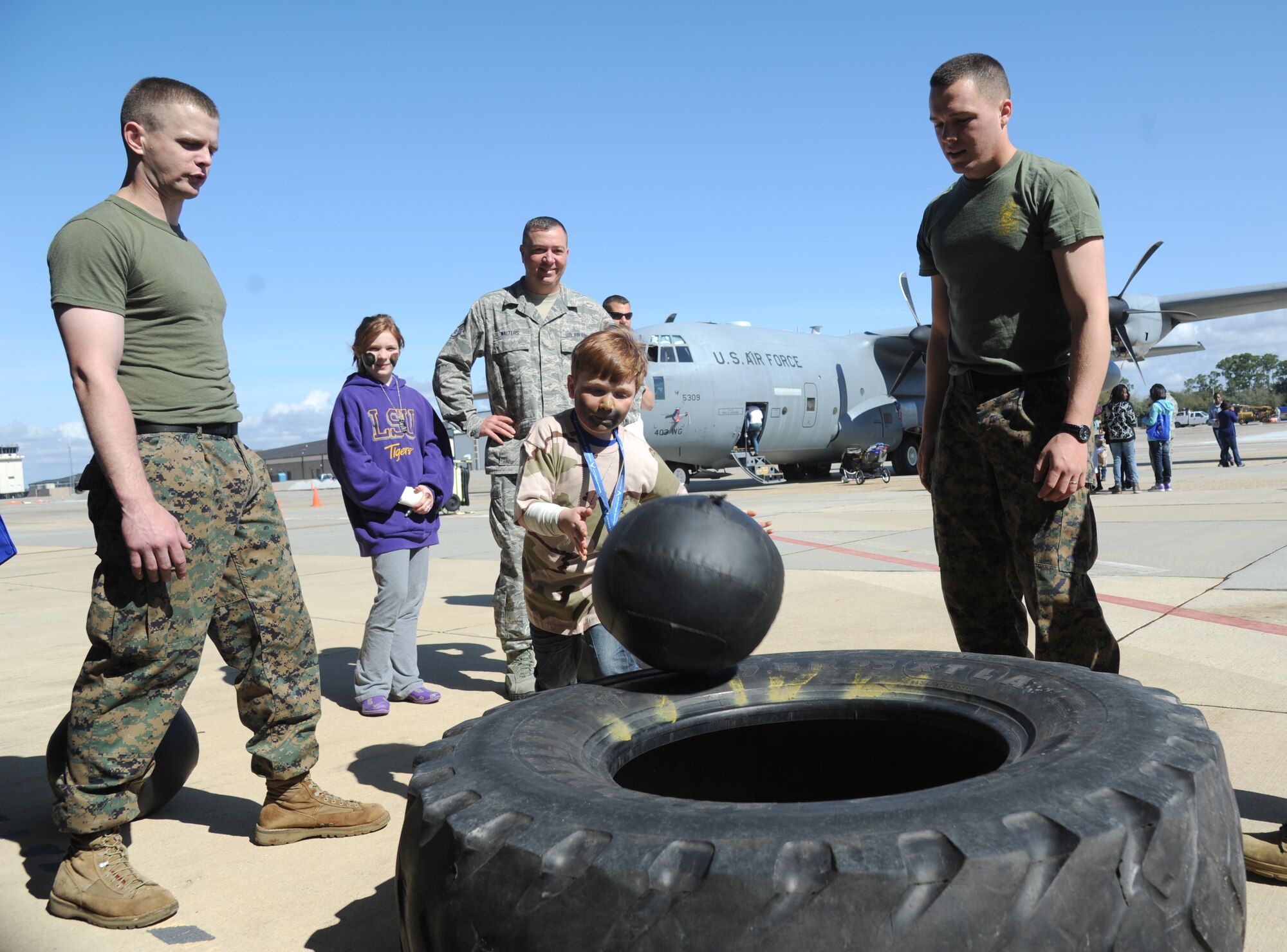 The son of staff Sgt. Travis Walters, 403rd Maintenance Squadron, throws a weight ball into the center of a tire as Keesler Marine Detachment Marines stand by during Operation Hero March 8, 2014, at Keesler Air Force Base, Miss.  The event was designed to help children better understand what happens when their parents deploy.  (U.S. Air Force photo by Kemberly Groue)