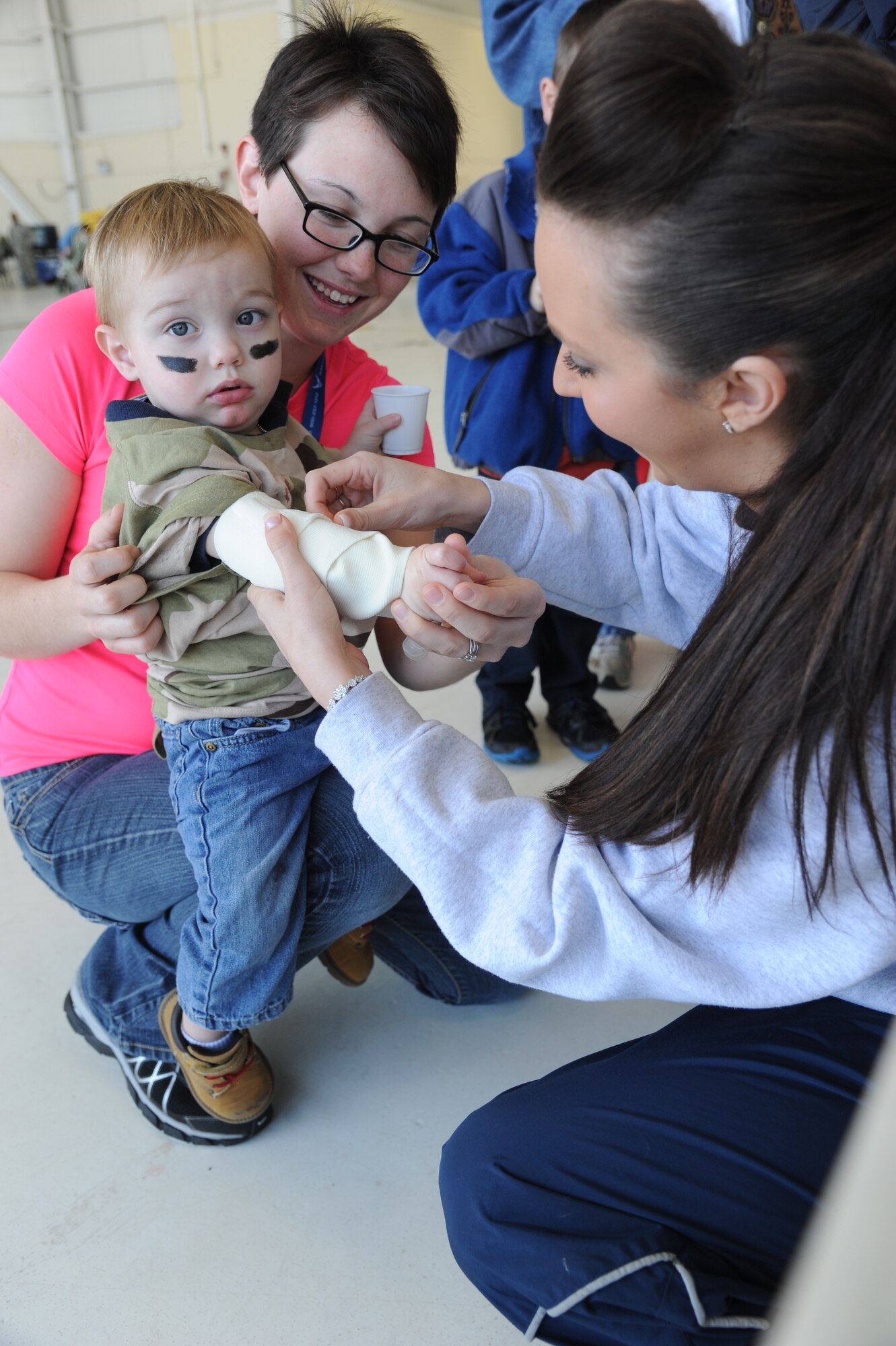Senior Airman Dana Rollins, 81st Diagnostic and Therapeutics Squadron, holds her son as Senior Airman Nichelle Patterson, 81st Aerospace Medicine Squadron, wraps his arm in gauze to simulate medical treatment during Operation Hero March 8, 2014, at Keesler Air Force Base, Miss.  The event was designed to help children better understand what happens when their parents deploy.  (U.S. Air Force photo by Kemberly Groue)