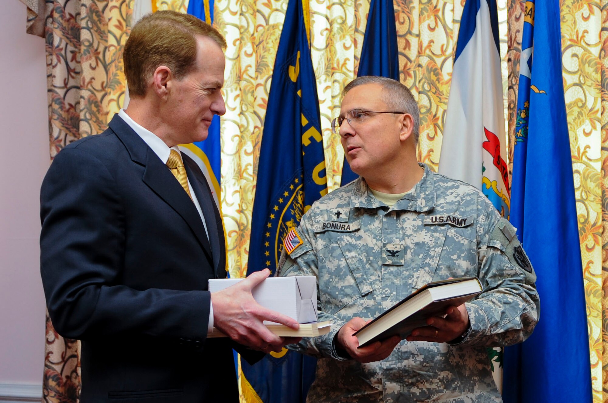 From right, U.S. Army Col. Dean Bonura, Regimental Memorial chapel chaplain, offers mementos to retired U.S. Army Maj. Gen. Bradley May during the 2014 National Prayer Breakfast at Fort Eustis, Va., March 6, 2014. The U.S. Army Training and Doctrine Command band played at the event. (U.S. Air Force photo by Senior Airman Austin Harvill/Released) (Photo cropped, color balanced, and contrast adjusted to enhance image)