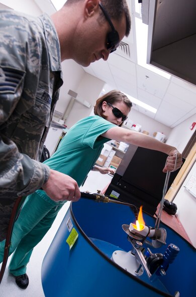 U.S. Air Force Tech. Sgt. Matthew Fitzgerald, 23d Aerospace Medicine Squadron NCO in charge of dental laboratory, and Senior Airman Julia Frensley, 23d AMDS dental assistant, casts a full, gold crown at Moody Air Force Base, Ga., March 6, 2014. The casting process includes melting the gold, encasing it in a plaster mold and sanding and polishing the crown. (U.S. Air Force photo by Senior Airman Tiffany M. Grigg/Released) 