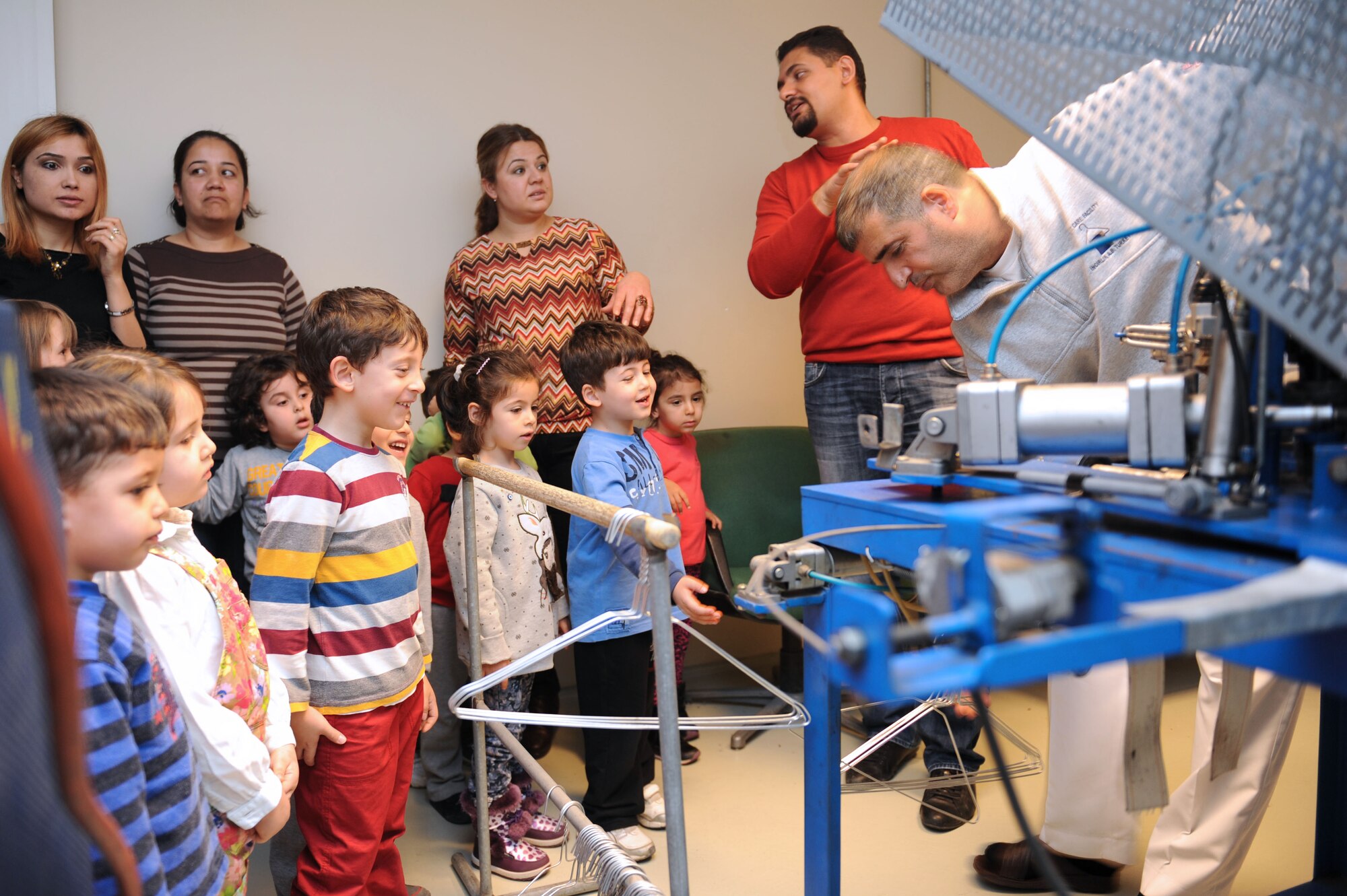 Turkish schoolchildren watch as Deniz Caliskan, 39th Force Support Squadron fabric care facility employee, shows how a wire-hanger crafting machine works Feb. 27, 2014, Incirlik Air Base, Turkey. The children received a tour of the full dry cleaning and washing facility, to include the machine workshop where the hanger machine was made. (U.S. Air Force photo by Senior Airman Chase Hedrick/Released)