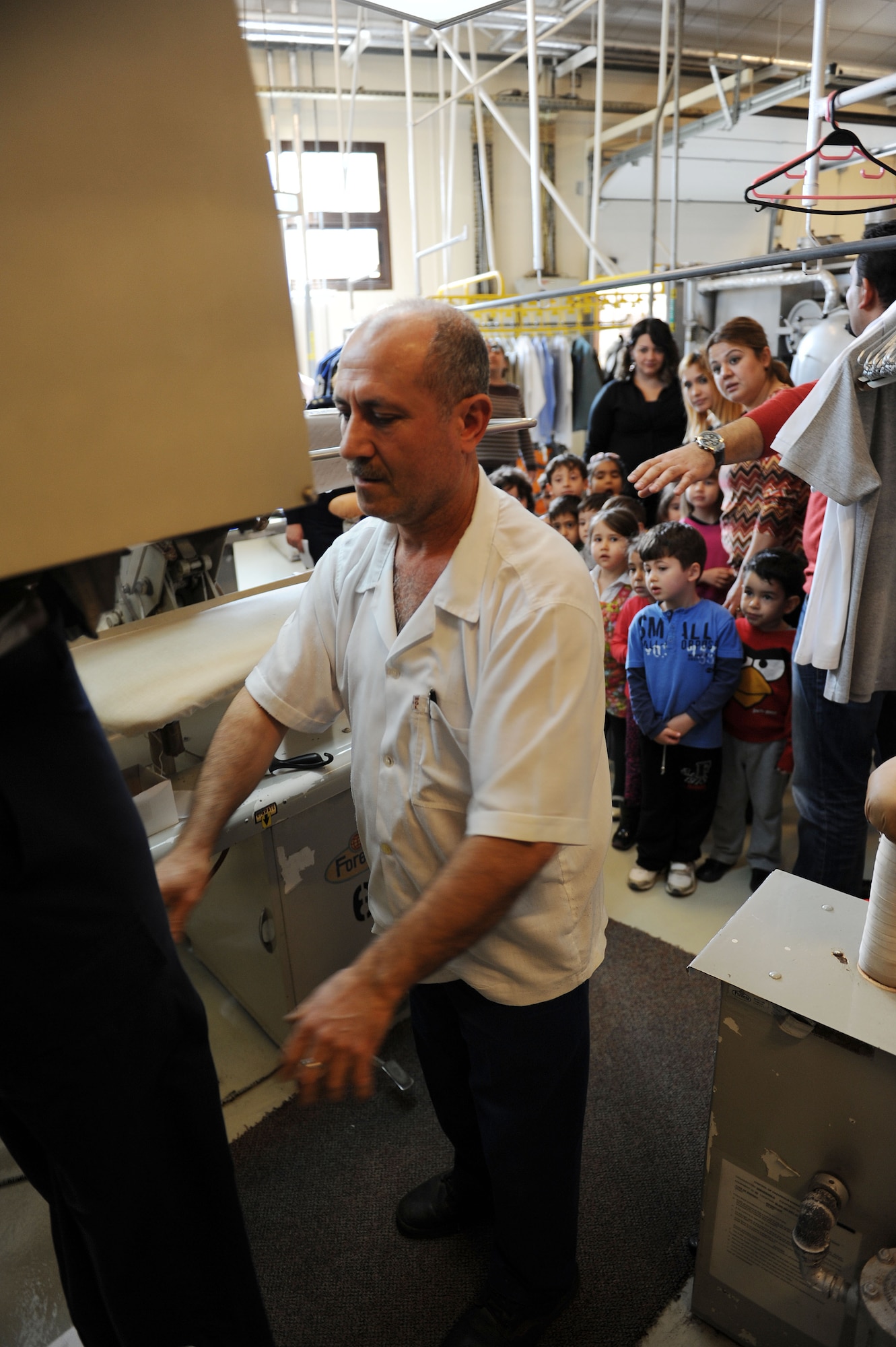 Numan Tanir, 39th Force Support Squadron fabric care facility foreman, demonstrates the dry cleaning process on pants to Turkish schoolchildren Feb. 27, 2014, Incirlik Air Base, Turkey. Some Incirlik Air Base facilities have begun giving tours to the children each week to give them a better understanding of what happens on the installation. (U.S. Air Force photo by Senior Airman Chase Hedrick/Released)