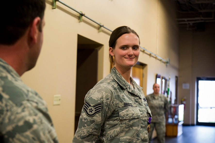 U.S. Air Force Staff Sgt. Haley Briggs, 824th Base Defense Squadron standards evaluation NCO in charge, shares a smile as Maj. Jeffrey Spencer, 824th BDS commander, speaks on her accomplishments during a Purple Heart Medal presentation ceremony March 12, 2014, at Moody Air Force Base, Ga. Briggs earned the medal from an August 2012 incident when she sustained injuries from an improvised explosive device while performing gunner duties outside of Bagram Airfield, Afghanistan. (U.S. Air Force photo by Staff Sgt. Jamal D. Sutter/Released)  
