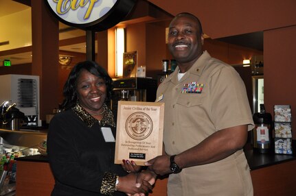 Capt. Marvin Jones, Naval Health Clinic Charleston commanding officer, presents Francine Bost, NHCC medical staff specialist, a plaque honoring her as NHCC Junior Civilian of the Year for 2013, during a ceremony March 7, 2014, at NHCC on Joint Base Charleston – Weapons Station, S.C. (U.S. Air Force illustration/Eric Sesit)