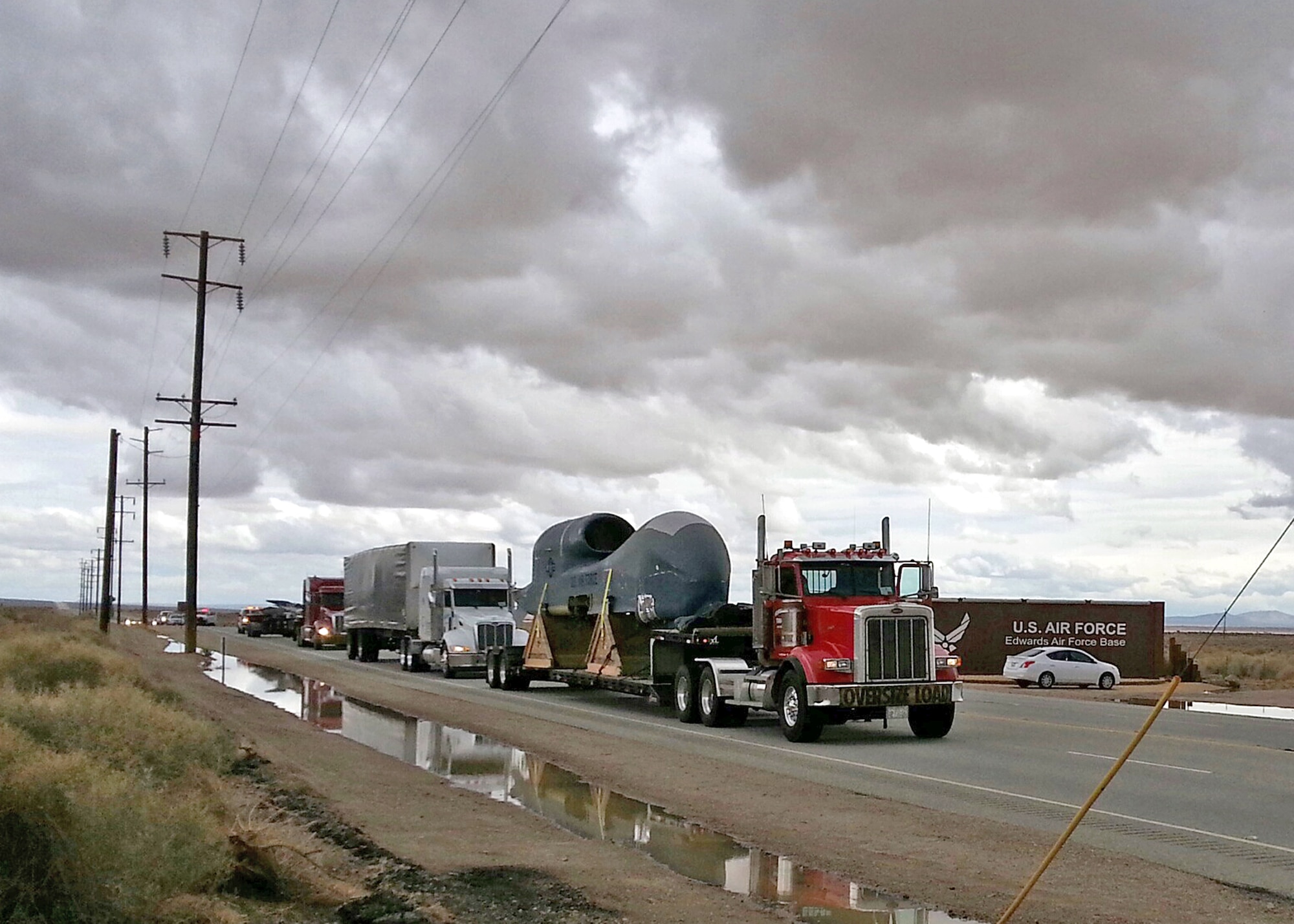 A 53-foot truck trailer transports an Edwards RQ-4B Global Hawk Block 20 remotely piloted aircraft (tail number 2016) through the Edwards AFB sign on Rosamond Blvd on Mar. 1. The Global Hawk T/N 2016 will be transferred to the Persistent Maritime Unmanned Aircraft Systems Program Office (PMA-262) located at Naval Air Station Patuxent River, Md., to be used in MQ-4C Triton device development and maintenance training. (U.S. Air Force photo by Derek Brown)