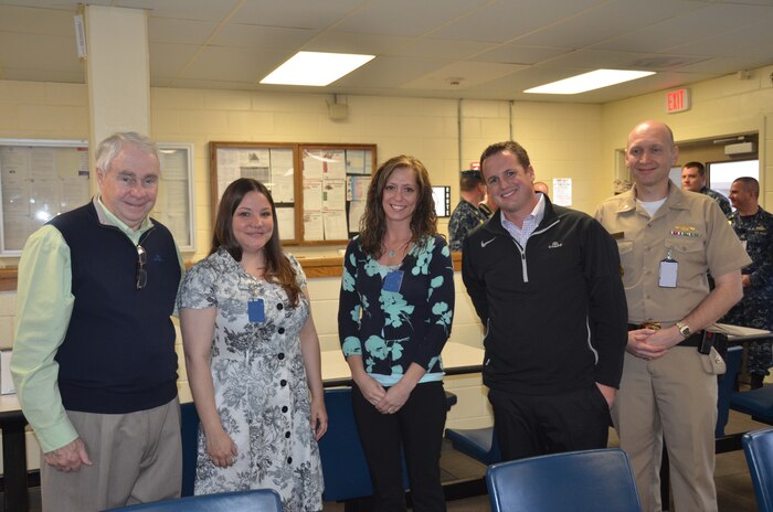 Commander Joseph Cole, Naval Consolidated Brig Charleston executive officer, hosts the Rotary Club of Daniel Island March 12, 2014, at the NCBC on Joint Base Charleston – Weapons Station, S.C. While visiting, Bill Stevens (left), President of the Rotary Club of Daniel Island, presented a check in the amount of $1,000 to Navy Marine Corps Relief Society representatives Annikah Moaratty, (second from left) and Sabrina Johnson, both NMCRS volunteer case workers. Additionally, Alex Jarvis (second from right), presented a check for $1,000 to the NMCRS on behalf of the Daniel Island Club. (U.S. Air Force illustration/Eric Sesit)