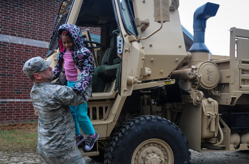 Senior Airman Richard Hill, 628th Medical Group medical material journeyman, helps a child down from a vehicle while visiting children at Eagle Nest Elementary during career day March 5, 2014. Four Airmen from the 628th MDG spoke with the children about the Air Force and their jobs. 