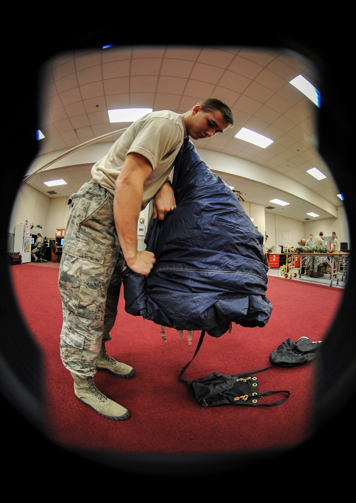 U.S. Air Force Airman 1st Class Elijah Chezem, 38th Rescue Squadron aircrew flight equipment apprentice, rolls a Vector parachute on Moody Air Force Base, Ga., March 11, 2014. Before packing the parachute, AFE personnel check for holes and make necessary repairs. (U.S. Air Force photo by Airman 1st Class Alexis Millican/Released)