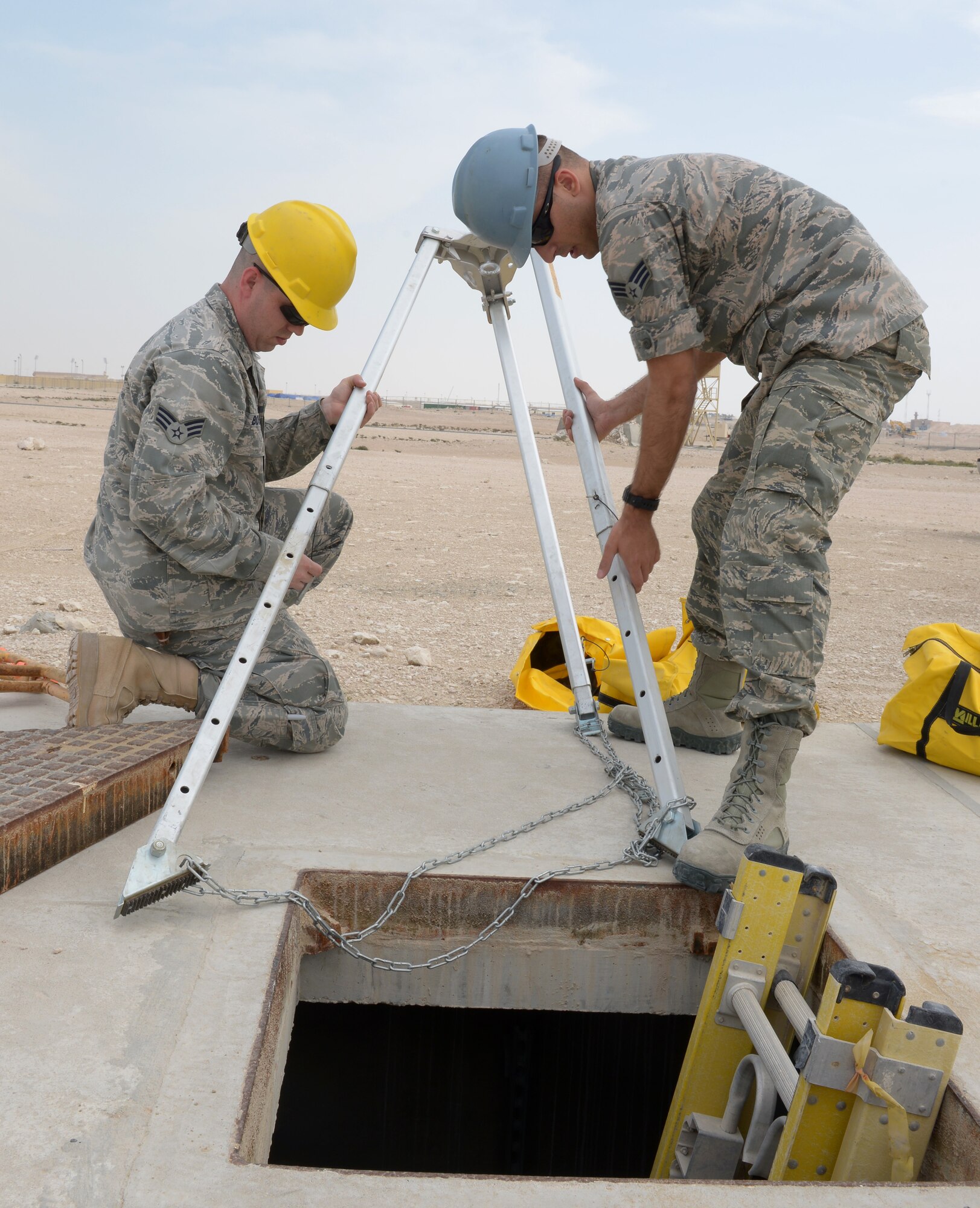 Senior Airmen Gary Boston and Michael Castglie set up a tripod at Al Udeid Air Base, Qatar, Mar. 10, 2014. The tripod is used as a safety measure to help lower an Airman into a manhole. Inside the manhole Airmen from the 379th Expeditionary Communications Squadron cable and antenna systems shop, or Cable Dawgs, maintain fiber optic cable used to run communication lines throughout the entire base. Both Airmen are 379th ECS cable and antenna systems technicians.  Boston is deployed from Barksdale Air Force Base, La., and an Oscoda, Mich., native. Castglie is deployed from Kadena Air Base, Japan, and a Brooklyn, N.Y., native. (U.S. Air Force photo/Senior Airman Hannah Landeros)