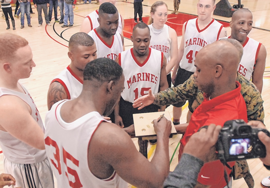Terrick Miller (35) is the first Marine Det. player to sign the bottom of the 2014 Commander’s Cup Basketball Tournament trophy, held by coach Billeetae Johnson following their 44-39 win over the 5th Engineer Battalion March 5 at DFC.
