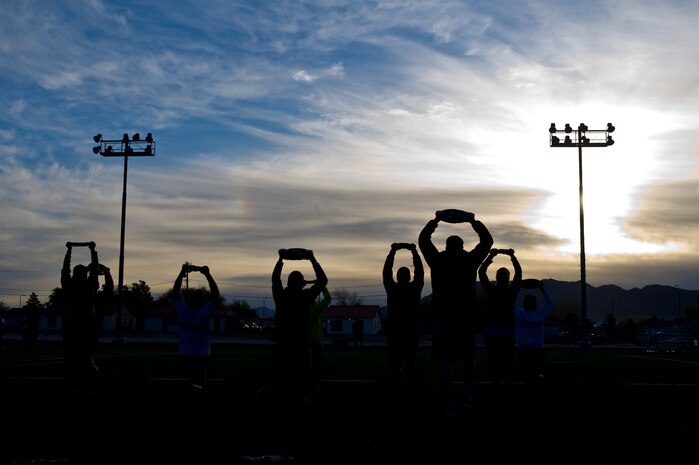 Warrior Trained Fitness workout participants, hold 25 pound weights over their heads while doing lunges on the field behind the Warrior Fitness Center, March 13, 2014 at Nellis Air Force Base, Nev.  This Warrior Trained Fitness workout consisted of eight exercise stations that focused on cardio and strength conditioning. (U.S. Air Force photo by Senior Airman Christopher Tam)