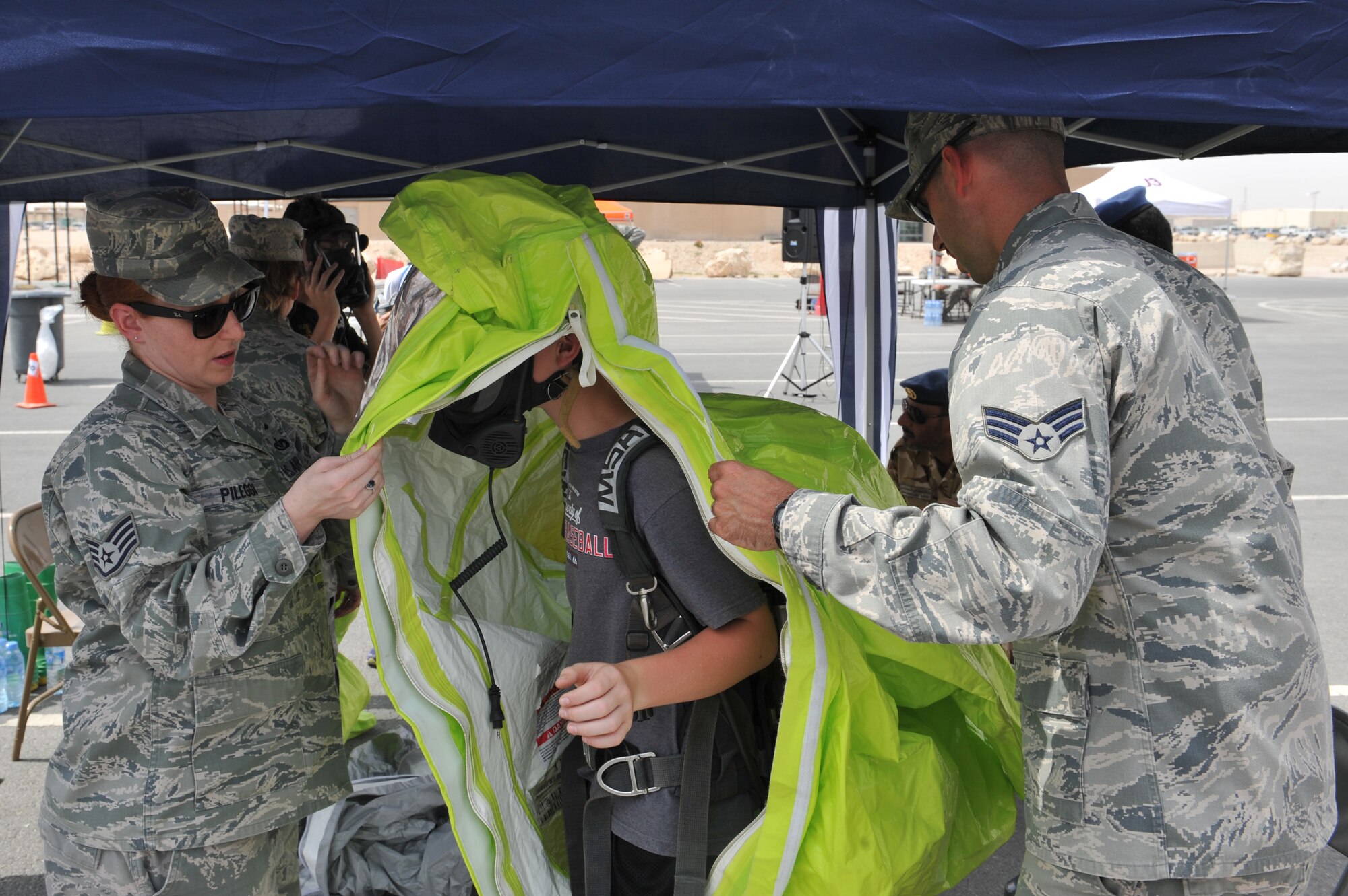 Staff Sgt. Stephanie Pileggi and Senior Airman Joe DeLullo help a student don a Level A suit which is a fully encapsulated hazardous materials suit that includes a self-contained breathing apparatus an air tank and face piece during the American School of Doha’s third annual 8th grade field trip to Al Udeid Air Base, Qatar, Mar. 10, 2014. The 379th Air Expeditionary Wing hosted a field trip for students showcasing the variety of careers available to Airmen. Around 150 students came to the base to see how Airmen live, where they work and exactly what they do. Pileggi and DeLullo are both 379th Expeditionary Civil Engineer Squadron readiness and emergency management journeymen. Pileggi is deployed from Scott Air Force base, Ill., and a New Smyrna Beach, Fl., native. DeLullo is deployed from Minot Air Force Base. N.D., and a native of Williamsport, Pa. (U.S. Air Force photo by Master Sgt. David Miller)