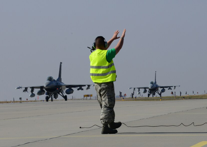 A 31st Aircraft Maintenance Squadron crew chief guides F-16 Fighting Falcons into place, March 14, 2014, at Lask Air Base, Poland. A total of twelve 555th Fighter Squadron F-16 Fighting Falcons and more than service members arrived to augment an off-site training event, which demonstrates an enduring partnership with NATO allies. (U.S. Air Force photo/Airman 1st Class Ryan Conroy) 
