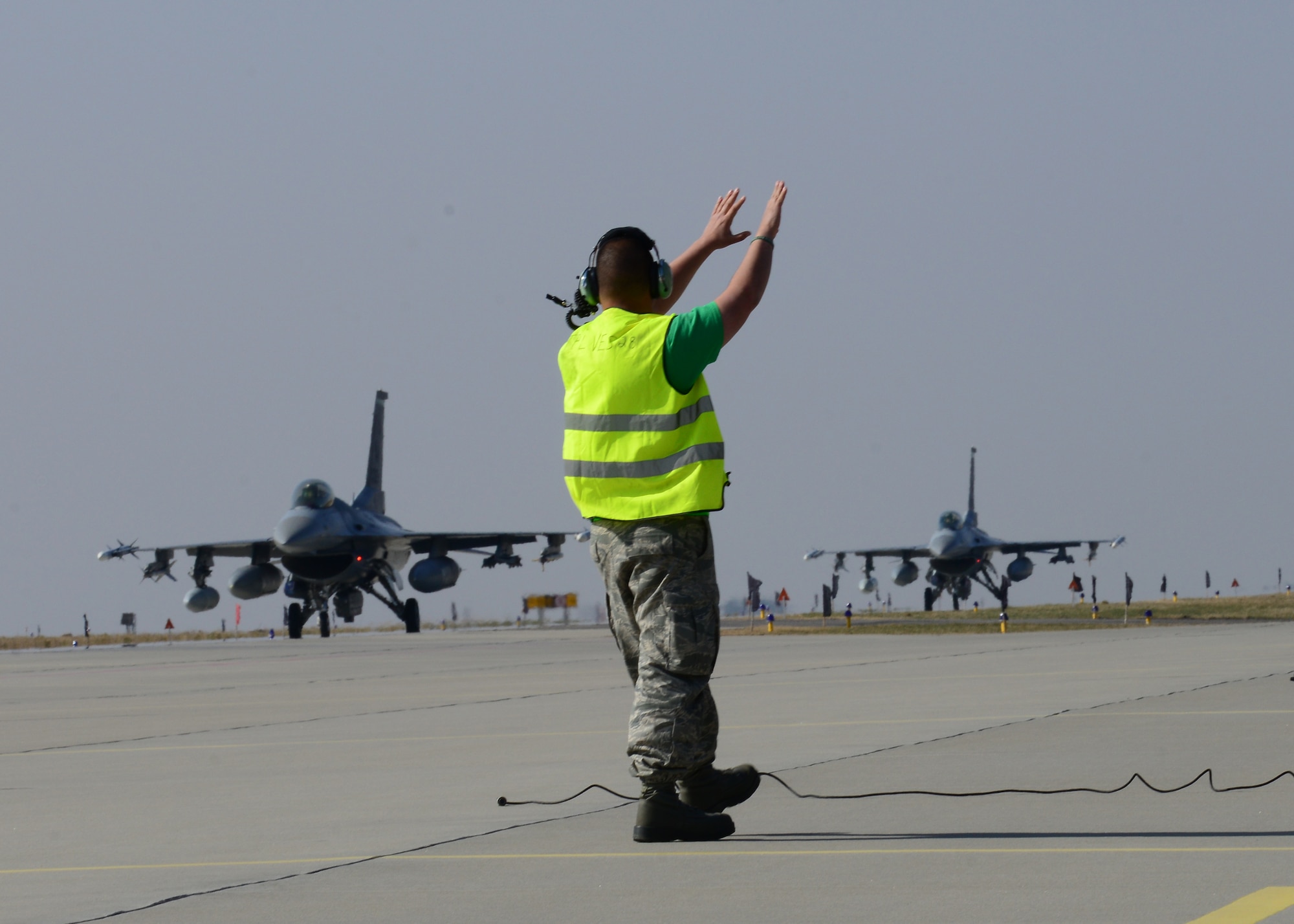A 31st Aircraft Maintenance Squadron crew chief guides 555th F-16 Fighting Falcons into place, March 14, 2014, at Lask Air Base, Poland. A total of twelve 555th Fighter Squadron F-16 Fighting Falcons and 200 military personnel arrived to augment an off-site training event, which demonstrates an enduring partnership with NATO allies. (U.S. Air Force photo/Airman 1st Class Ryan Conroy) 