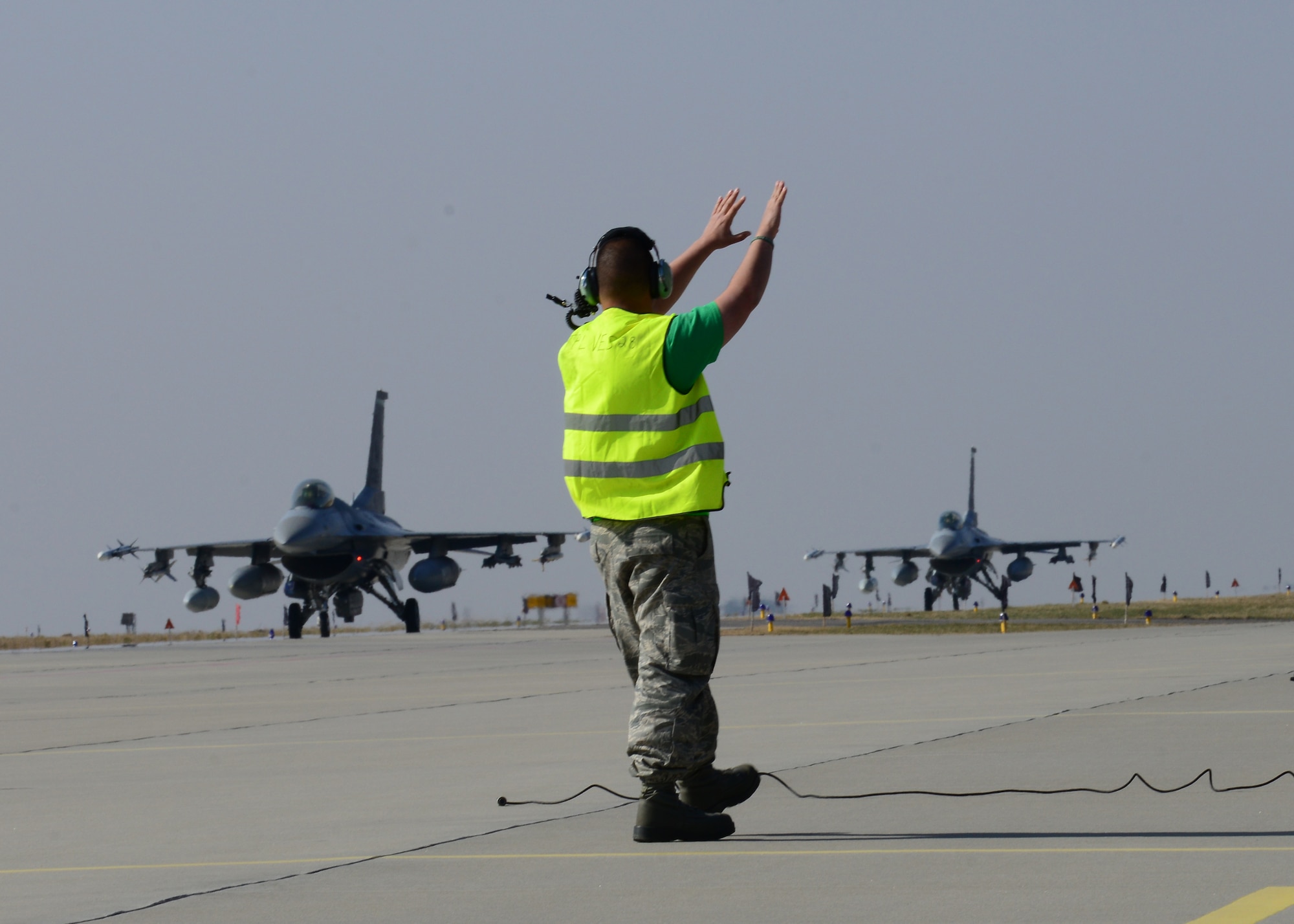 A 31st Aircraft Maintenance Squadron crew chief guides 555th F-16 Fighting Falcons into place, March 14, 2014, at Lask Air Base, Poland. A total of twelve 555th Fighter Squadron F-16 Fighting Falcons and 200 military personnel arrived to augment an off-site training event, which demonstrates an enduring partnership with NATO allies. (U.S. Air Force photo/Airman 1st Class Ryan Conroy) 

