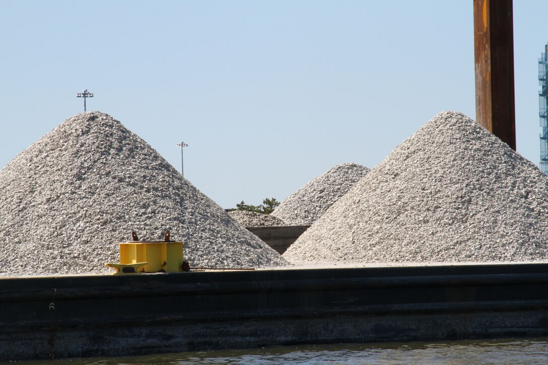 Mounds of fossilized oyster shell are staged on barges to be placed on the Lafayette River oyster reef, marked by white poles in the water.