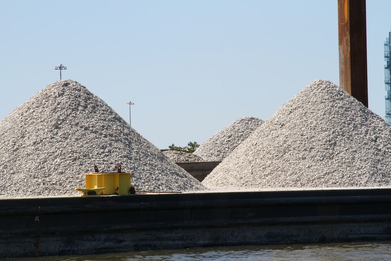 Mounds of fossilized oyster shell are staged on barges to be placed on the Lafayette River oyster reef, marked by white poles in the water.