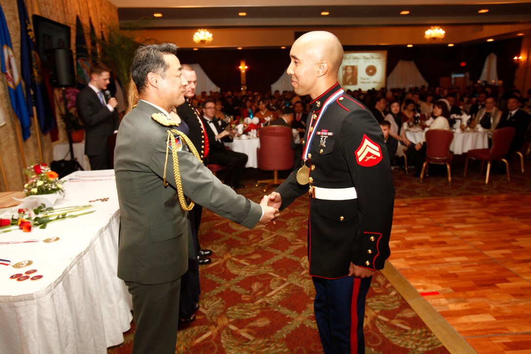 – Japan Ground Self-Defense Force Maj. Gen. Shigeru Kobayashi, left, shakes hands with U.S. Marine Cpl. Michael S. Williamson during the 43rd annual USO Service Salute March 8 at the Butler Officers’ Club on Camp Foster. Williamson was among seven Japan Self-Defense Force and U.S. service members recognized for volunteer efforts and community support. Kobayashi is the commanding general of the 15th Brigade, Western Army. Williamson is a field artillery radar operator with Headquarters Battery, 12th Marine Regiment, 3rd Marine Division, III Marine Expeditionary Force.